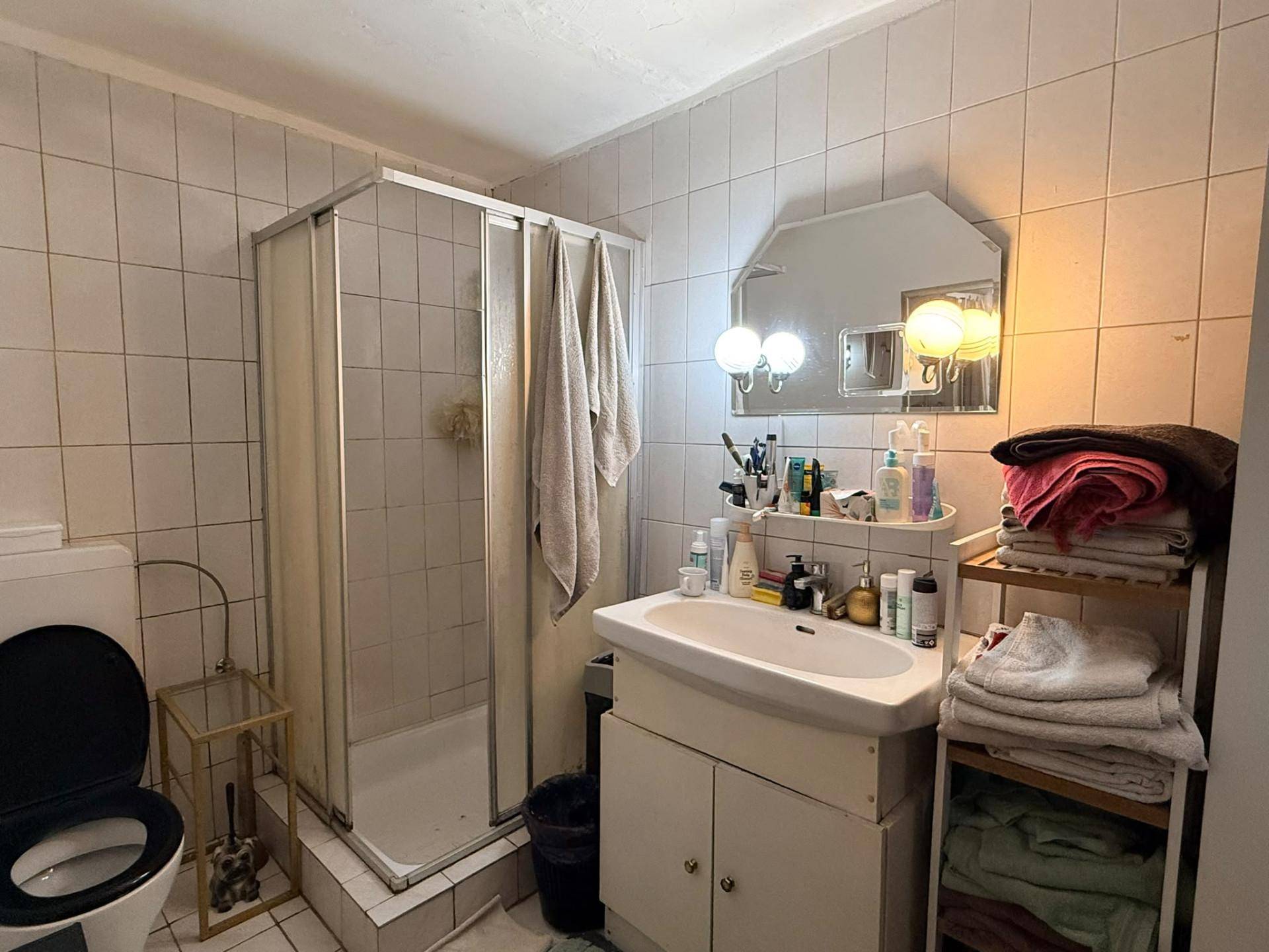 Badezimmer mit Duschkabine, Waschbecken und WC, hell gefliest und funktional eingerichtet im 80er-Jahre-Stil.