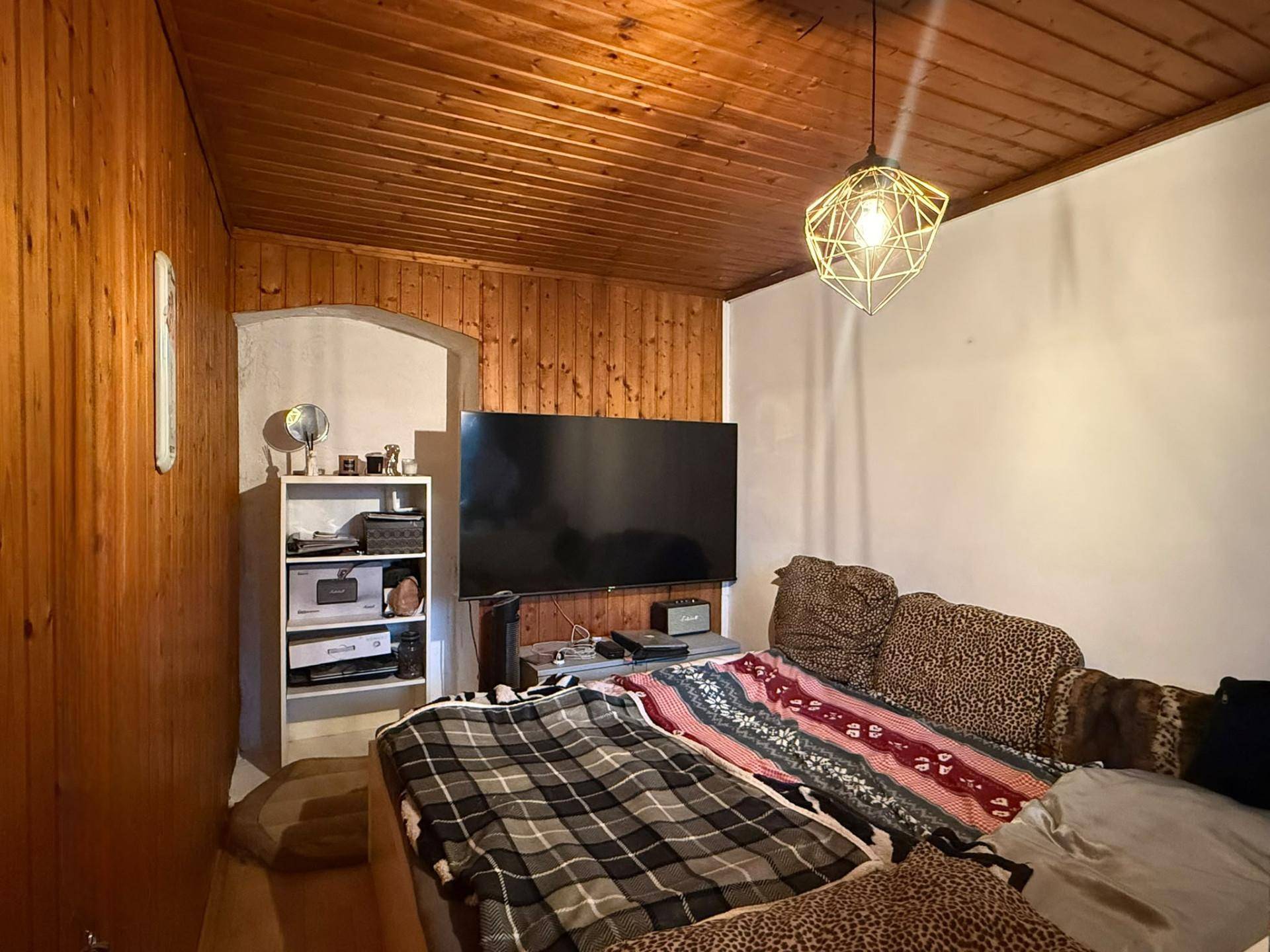 Wohnzimmer mit Holzvertäfelung, Fernseher und Sofa, in warmem Licht beleuchtet, gemütlich gestaltet.