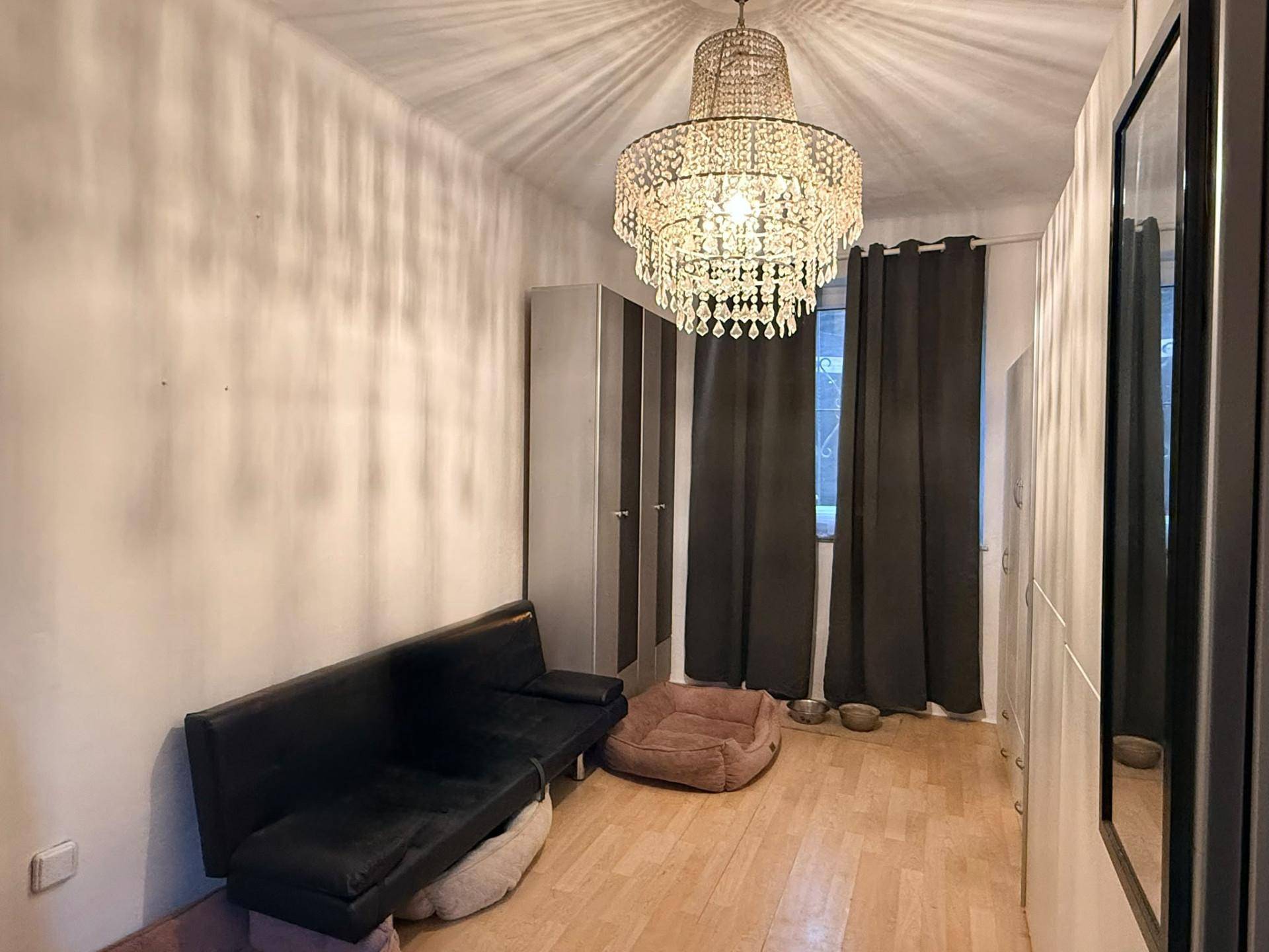 Zimmer mit Sofa, Kleiderschrank und Kronleuchter, mit Holzboden und dunklen Vorhängen, elegant beleuchtet.
