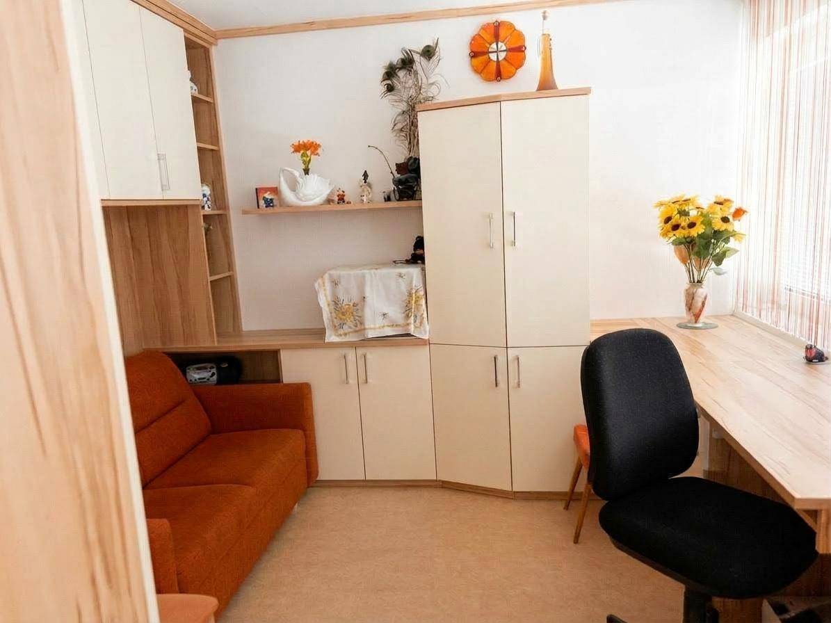 Heller Raum mit orangefarbenem Sofa, großem Schreibtisch und praktischen Einbauschränken am Fenster.