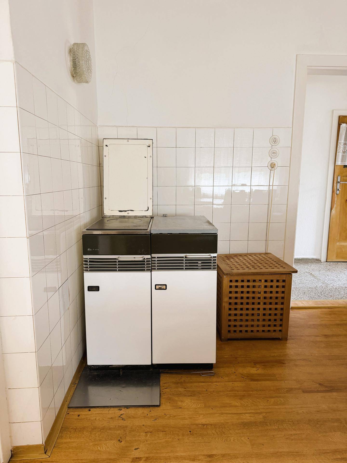 Alter Ofen mit weißen Fliesen an der Wand in einem funktionalen Raum mit Holzboden.