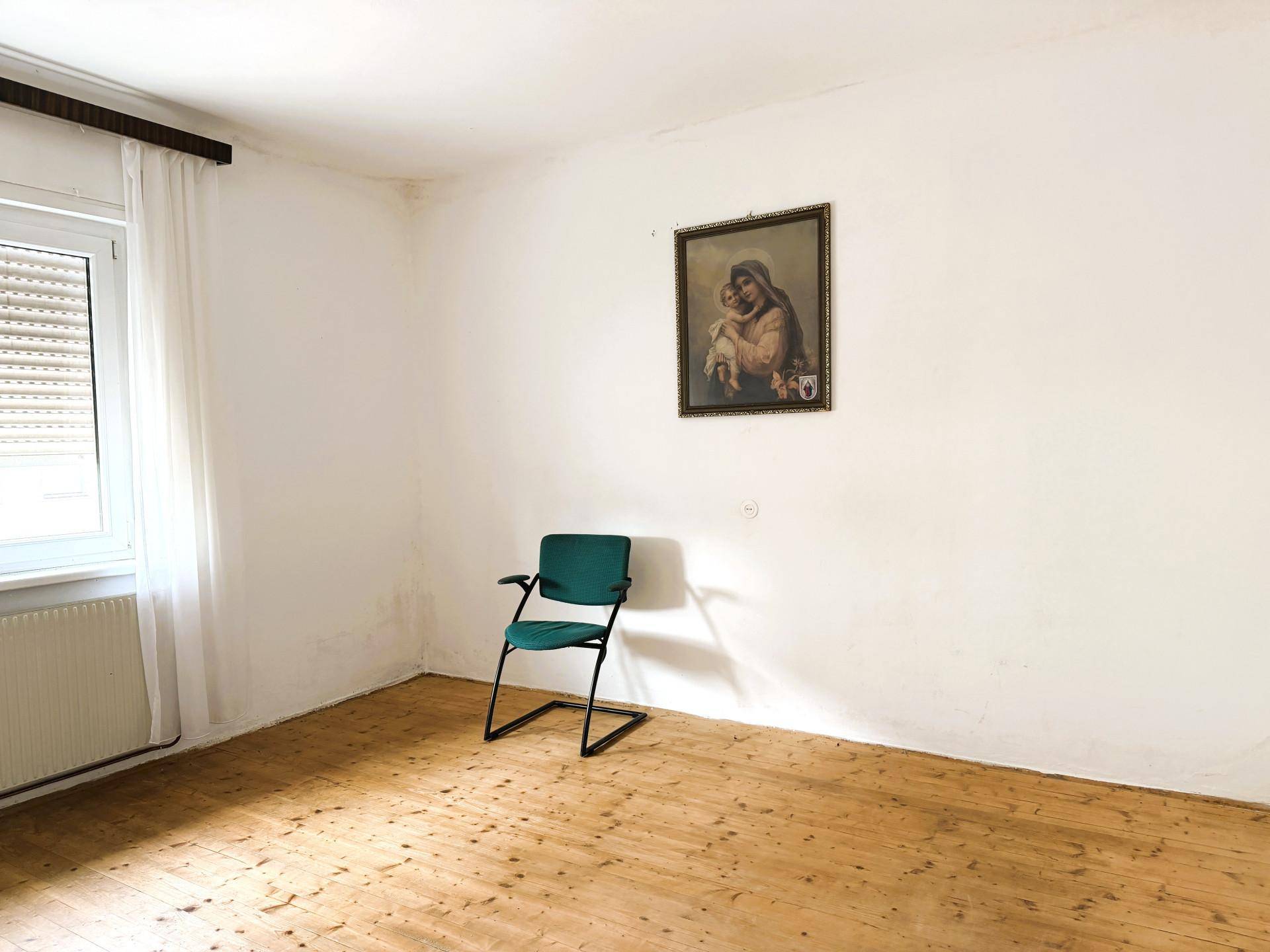 Leeres Zimmer mit Holzdielenboden und einem Fenster mit Rollladen, bereit zur individuellen Gestaltung.