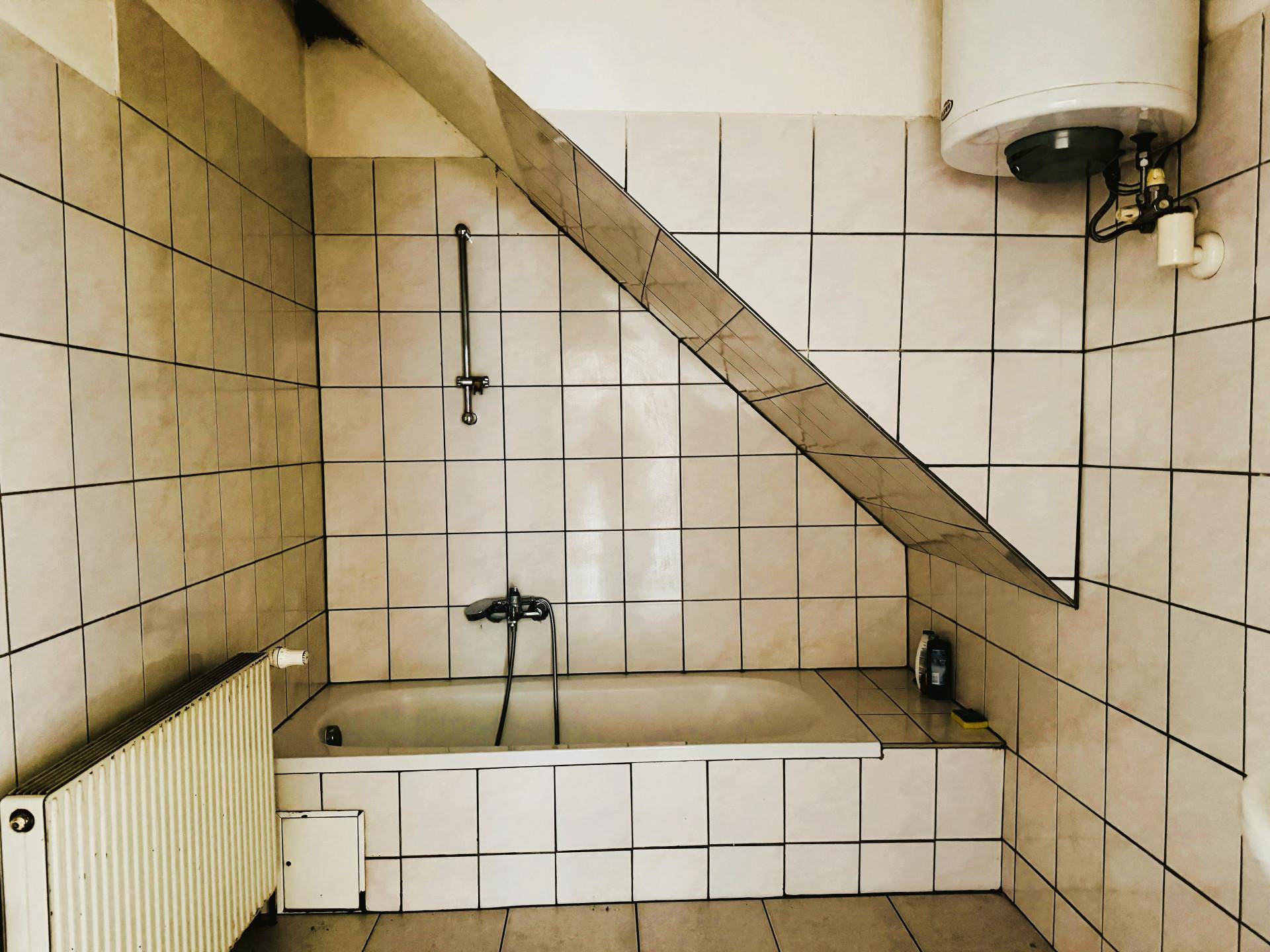 Gefliestes Badezimmer mit Badewanne, Dusche und Warmwasserboiler unter einer Dachschräge.