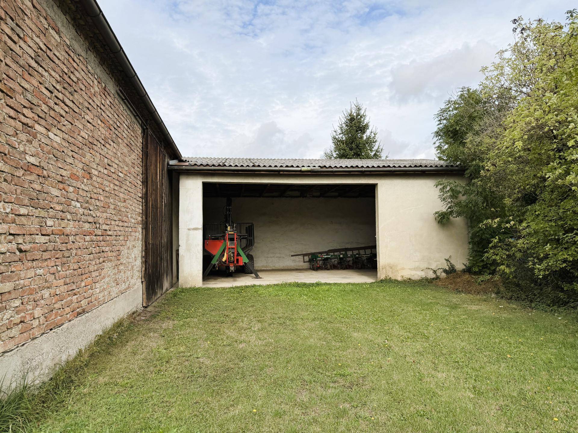Offene Garage oder Schuppen neben einem Ziegelgebäude auf einem grünen Grundstück.