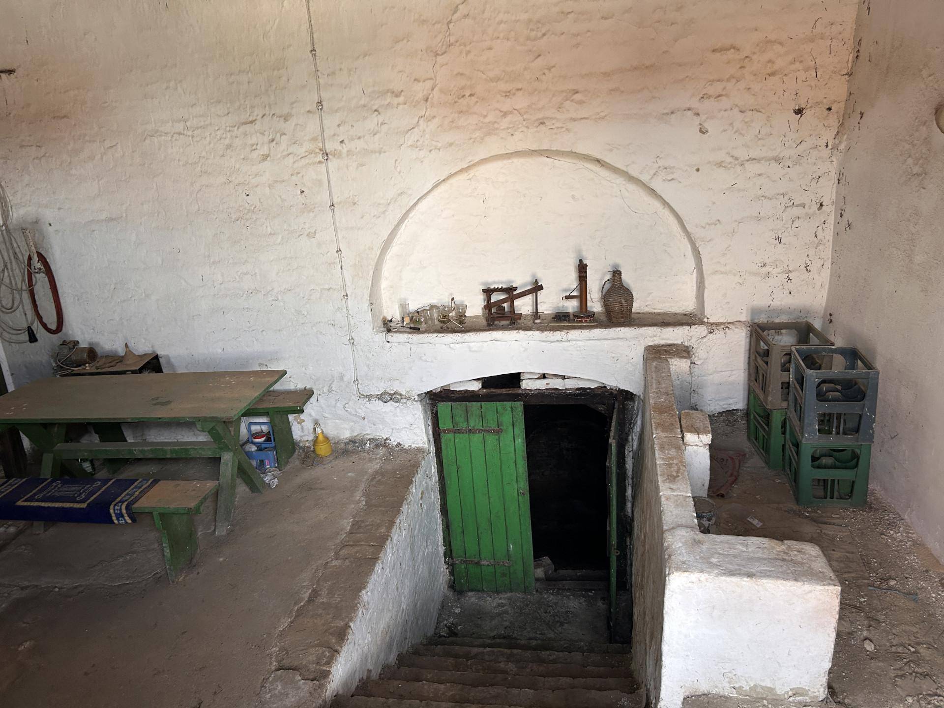 Alter Kellerraum mit Treppenabgang, Holztisch und einer gewölbten Nische, die historische Gegenstände zeigt.