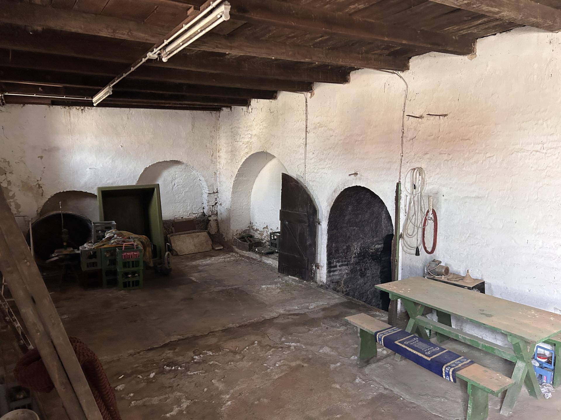 Geräumiger Kellerraum mit sichtbaren Holzbalken an der Decke, gewölbten Nischen und rustikalen Sitzgelegenheiten.