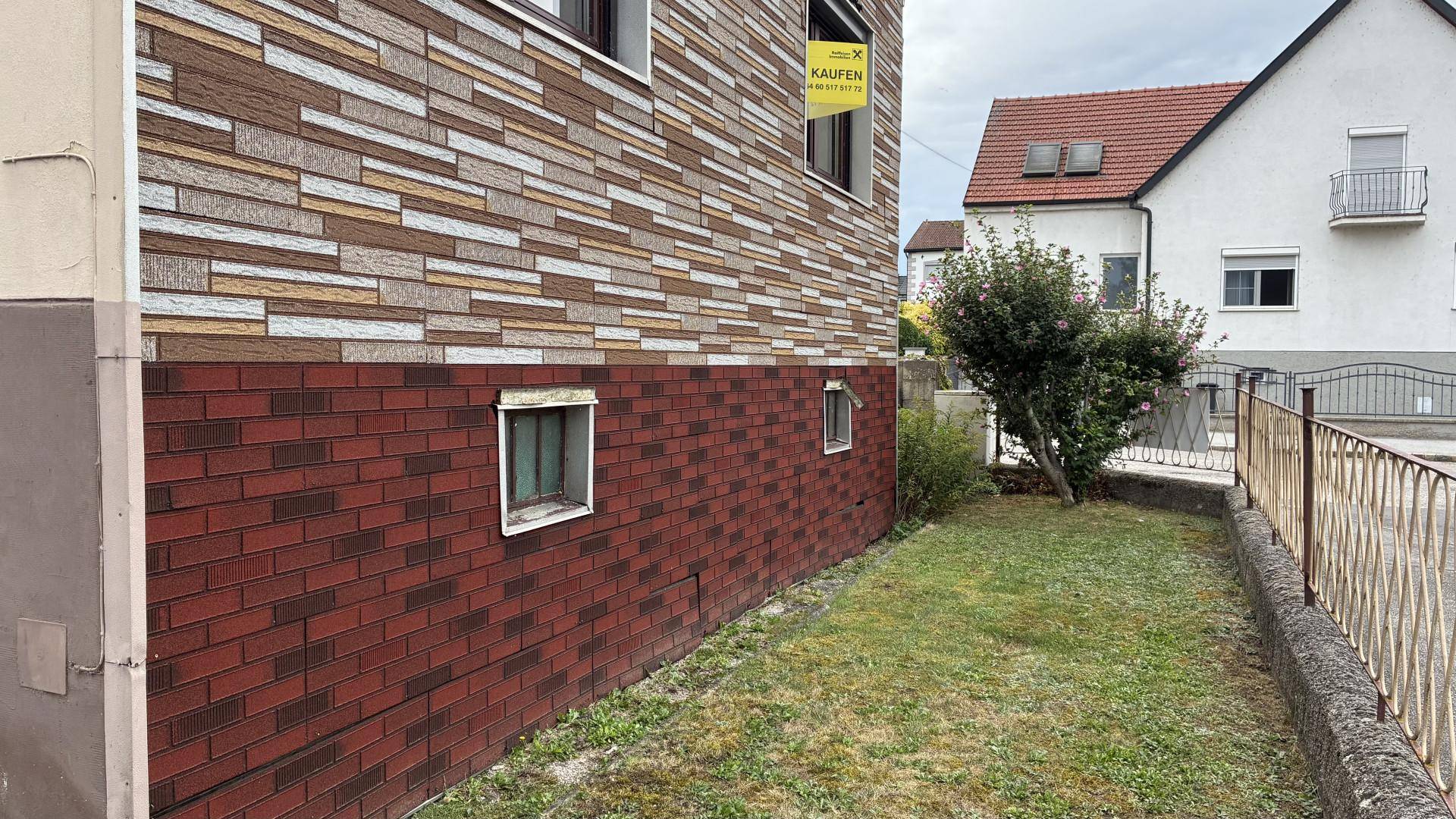 Seitenfassade des Hauses mit Ziegelverkleidung im unteren Bereich und kleinem Rasenstreifen.