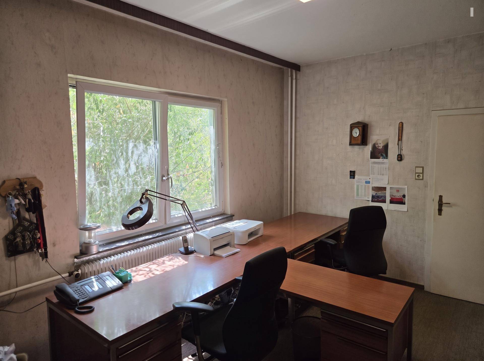 Geräumiges Büro mit zwei Arbeitsplätzen, großem Fenster und Blick auf Bäume.