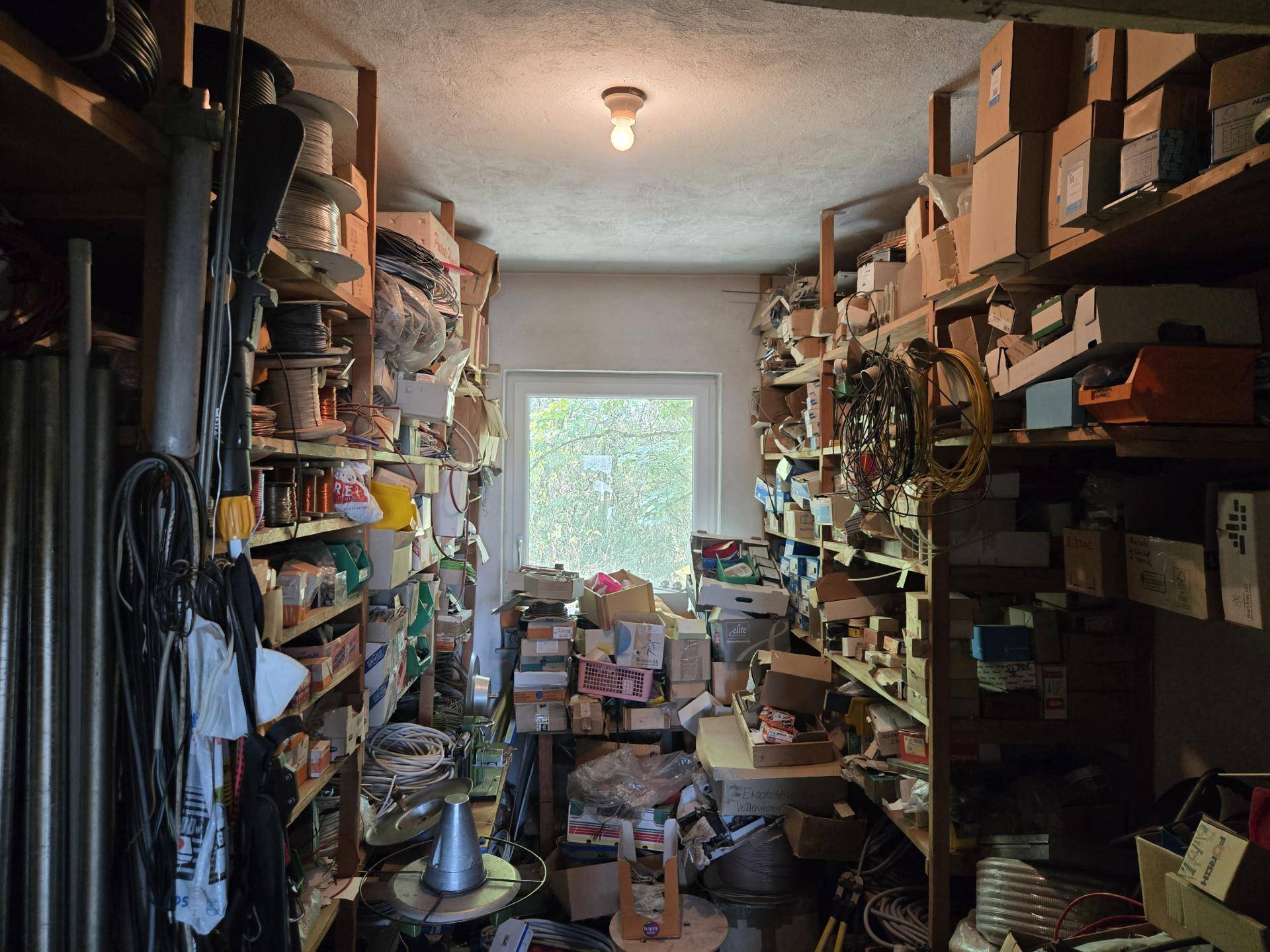Vollgestopfter Lagerraum mit Regalen voller Kartons, Kabeln und verschiedenen Materialien.