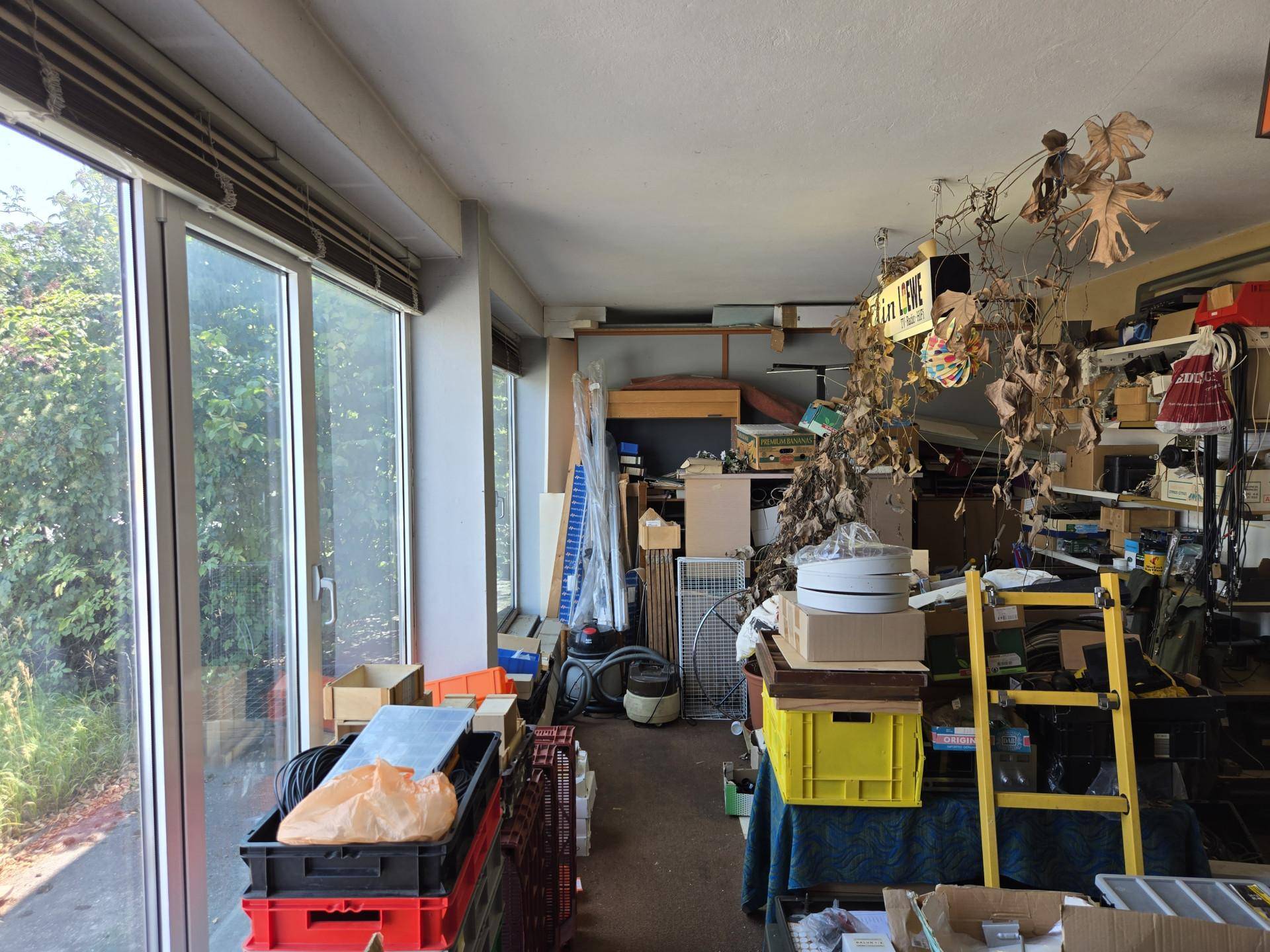 Großer Raum mit bodentiefen Fenstern, gefüllt mit verschiedenen Gegenständen und Dekorationen.