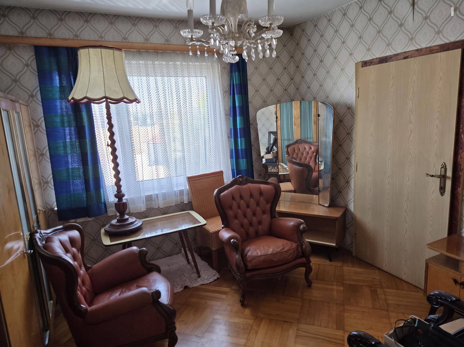 Gemütliches Wohnzimmer mit Parkettboden, zwei Sesseln, Stehlampe und gemusterter Tapete.