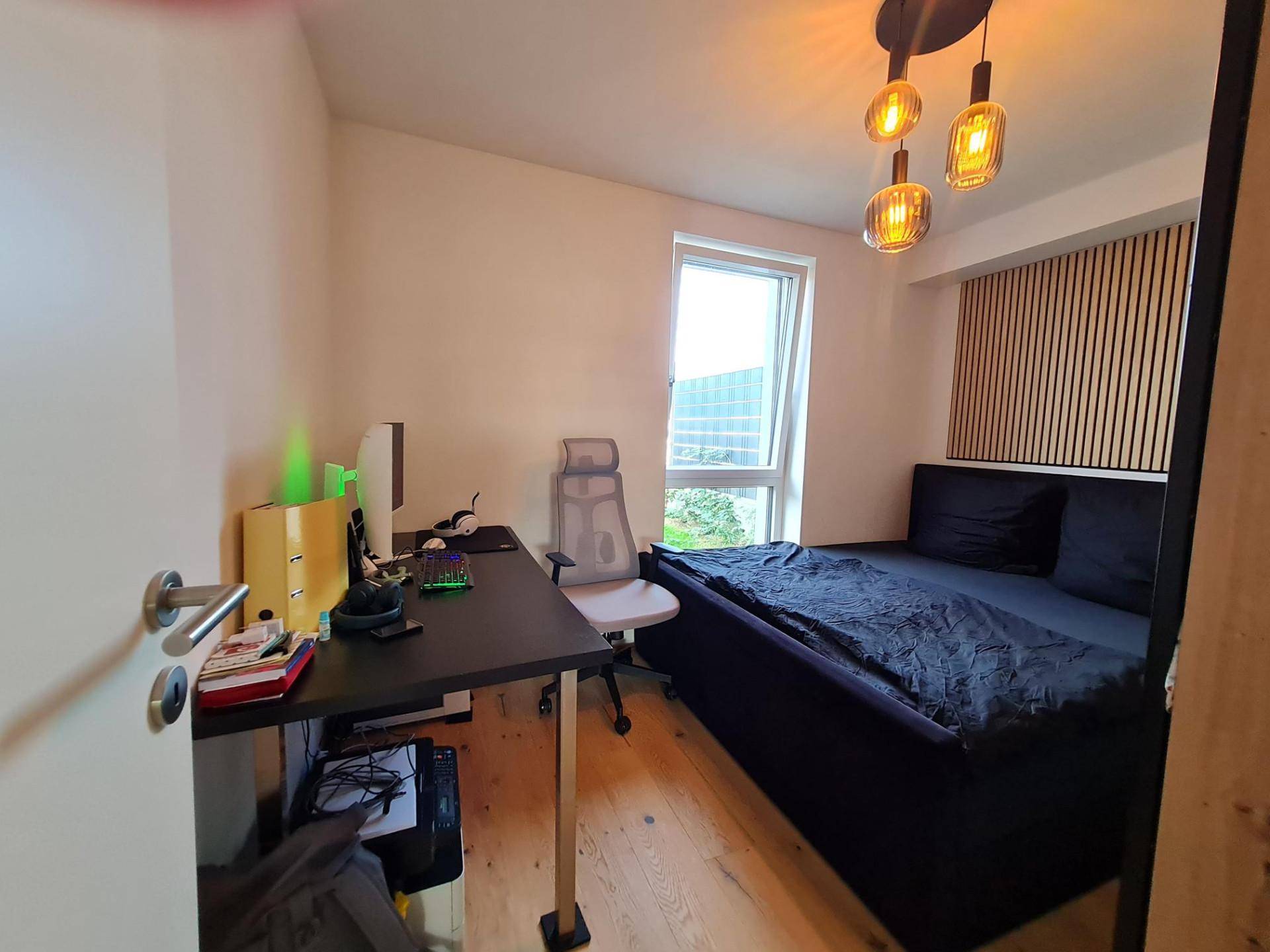 Funktionales Schlafzimmer mit Schreibtisch, Bett und dekorativer Holzlamellenwand.