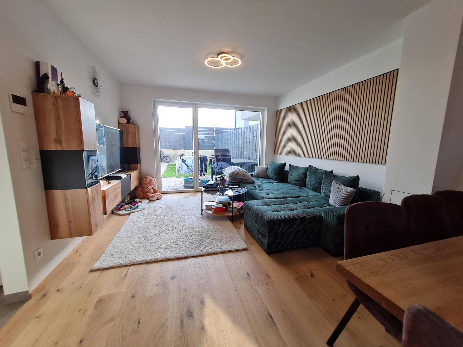 Gemütliches Wohnzimmer mit großem grünen Sofa, Holzboden und Zugang zur Terrasse.