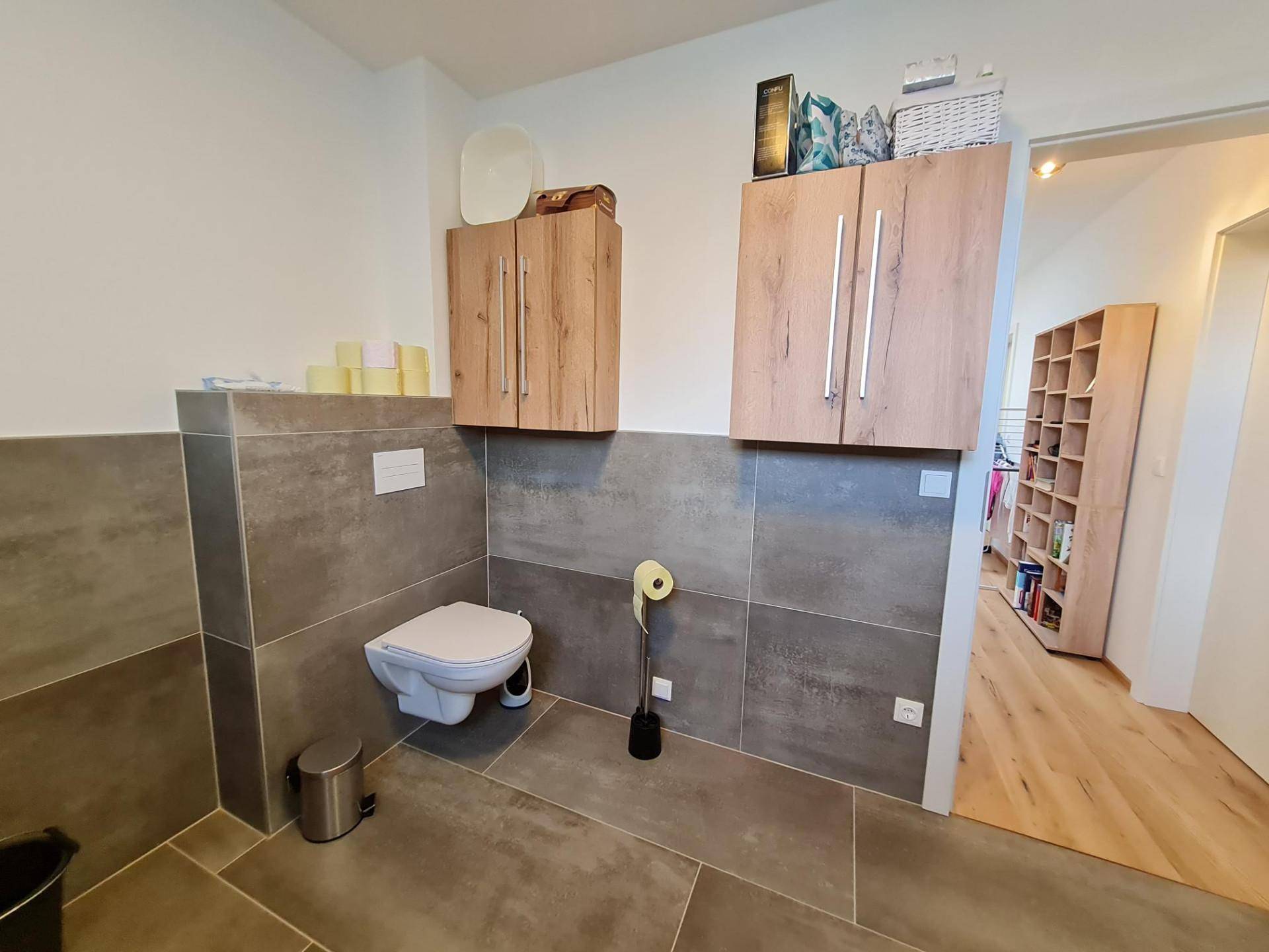 Badezimmer mit wandhängendem WC, Holzschränken und modernen Fliesen.