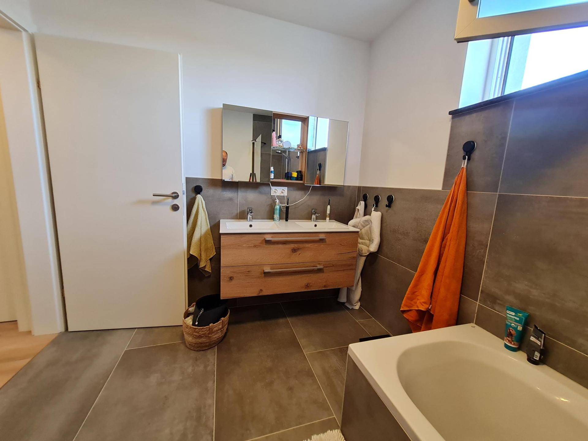 Modernes Badezimmer mit Doppelwaschbecken, Badewanne und großformatigen Fliesen.