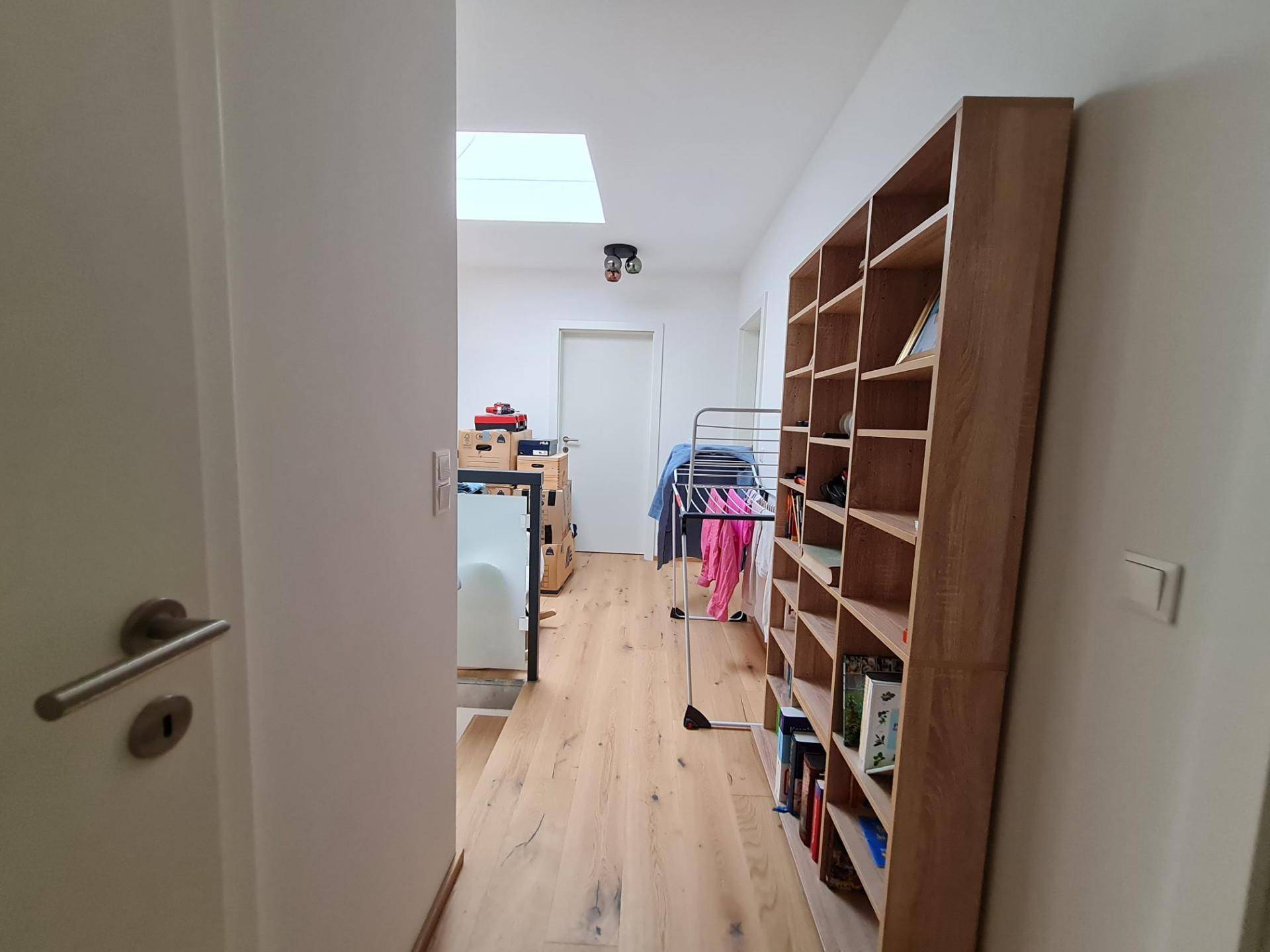 Lichtdurchfluteter Flur mit Bücherregal, Holzboden und Dachfenster.