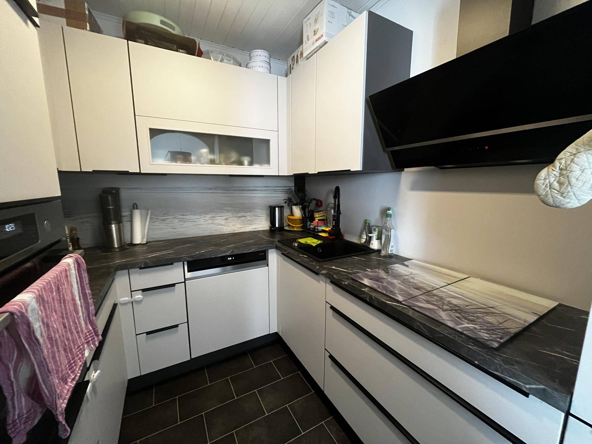 Moderne Küche mit weißen Hochglanzfronten, dunkler Arbeitsplatte und Induktionskochfeld.