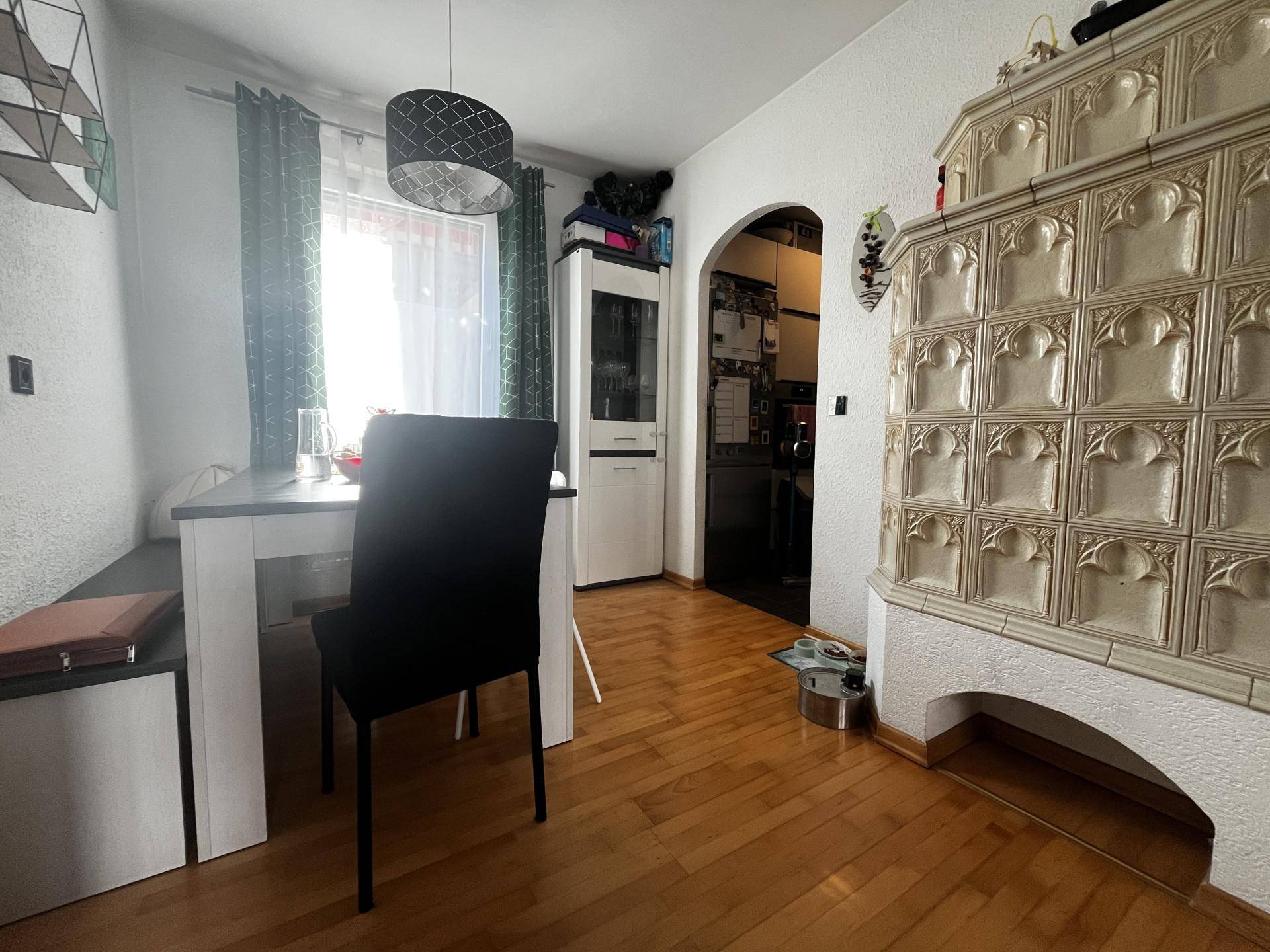 Gemütlicher Essbereich mit Holzboden, Esstisch und einem traditionellen Kachelofen.