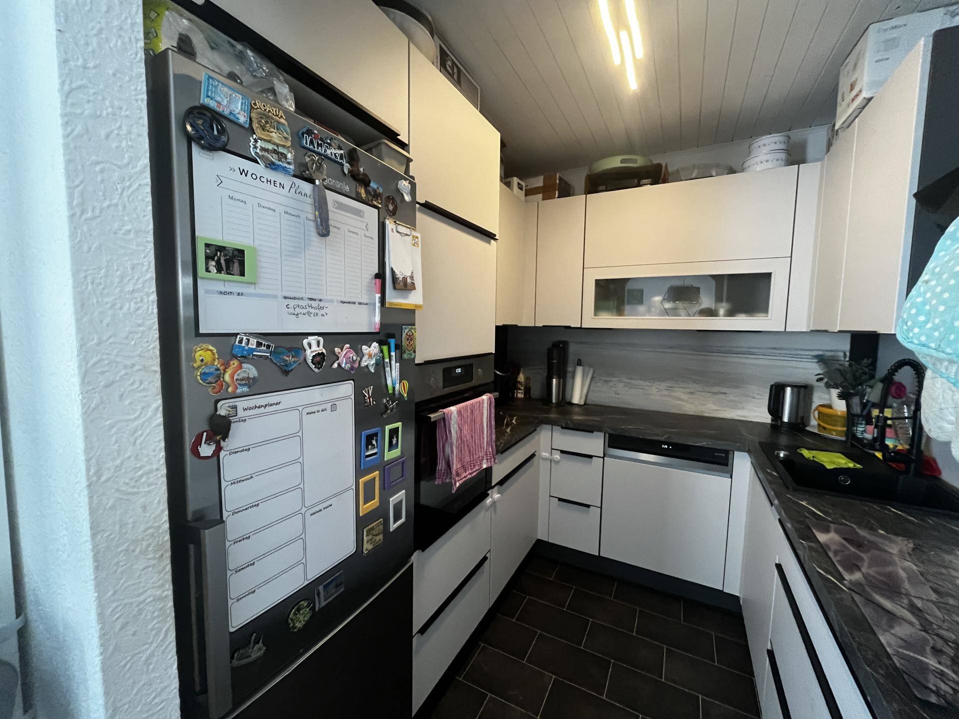Funktionale Küche mit integriertem Kühlschrank, weißen Schränken und dunklem Fliesenboden.