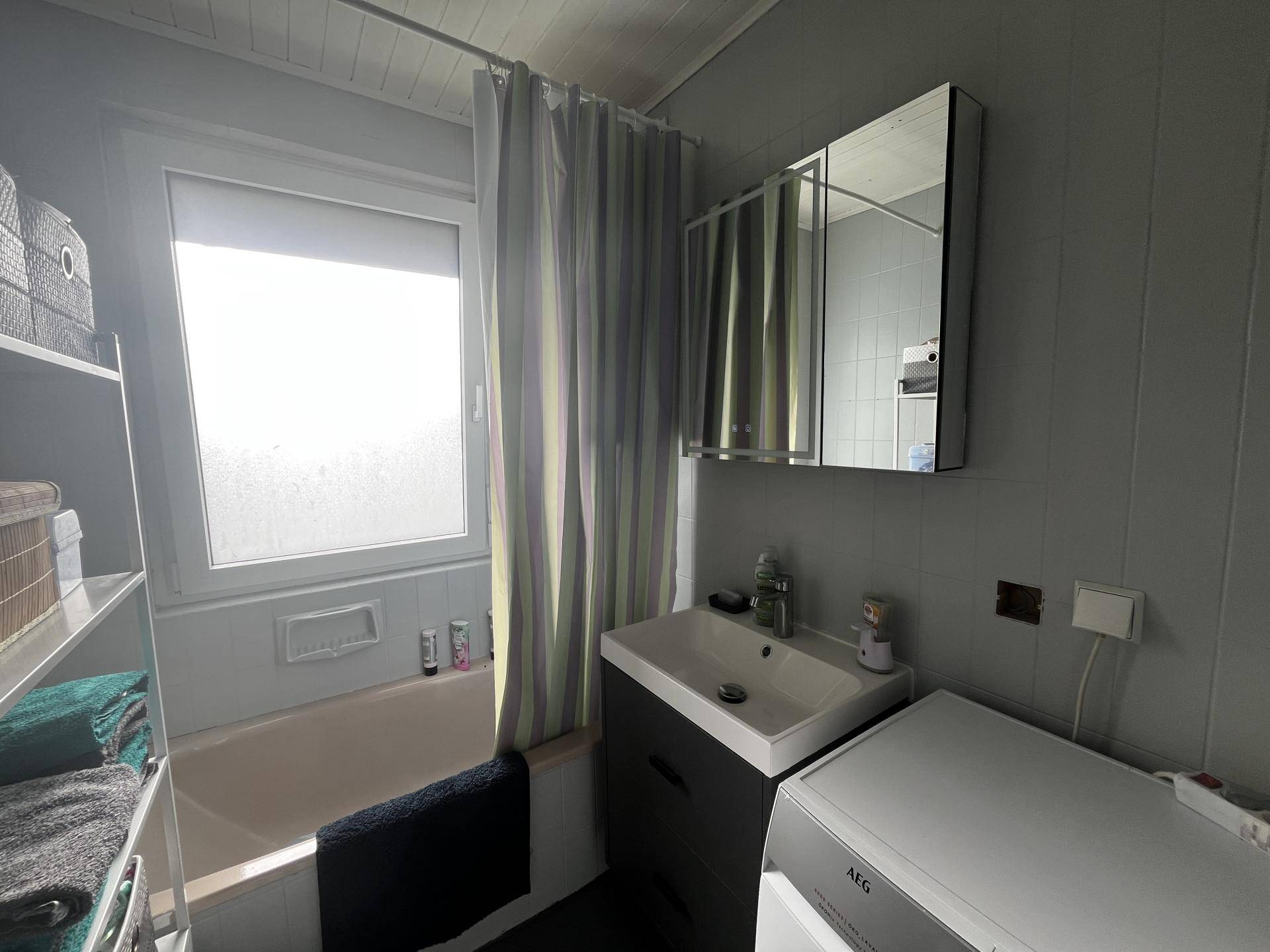 Badezimmer mit Badewanne, Duschvorhang, Fenster und Waschbeckenunterschrank.