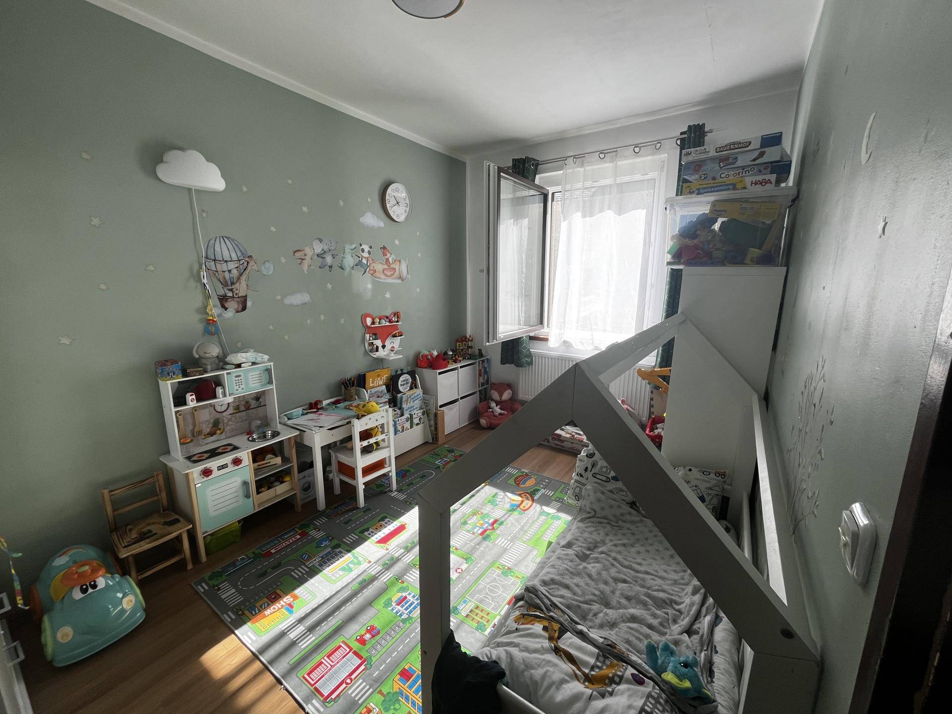 Helles Zimmer mit Holzboden, Spielteppich und kindgerechter Dekoration.