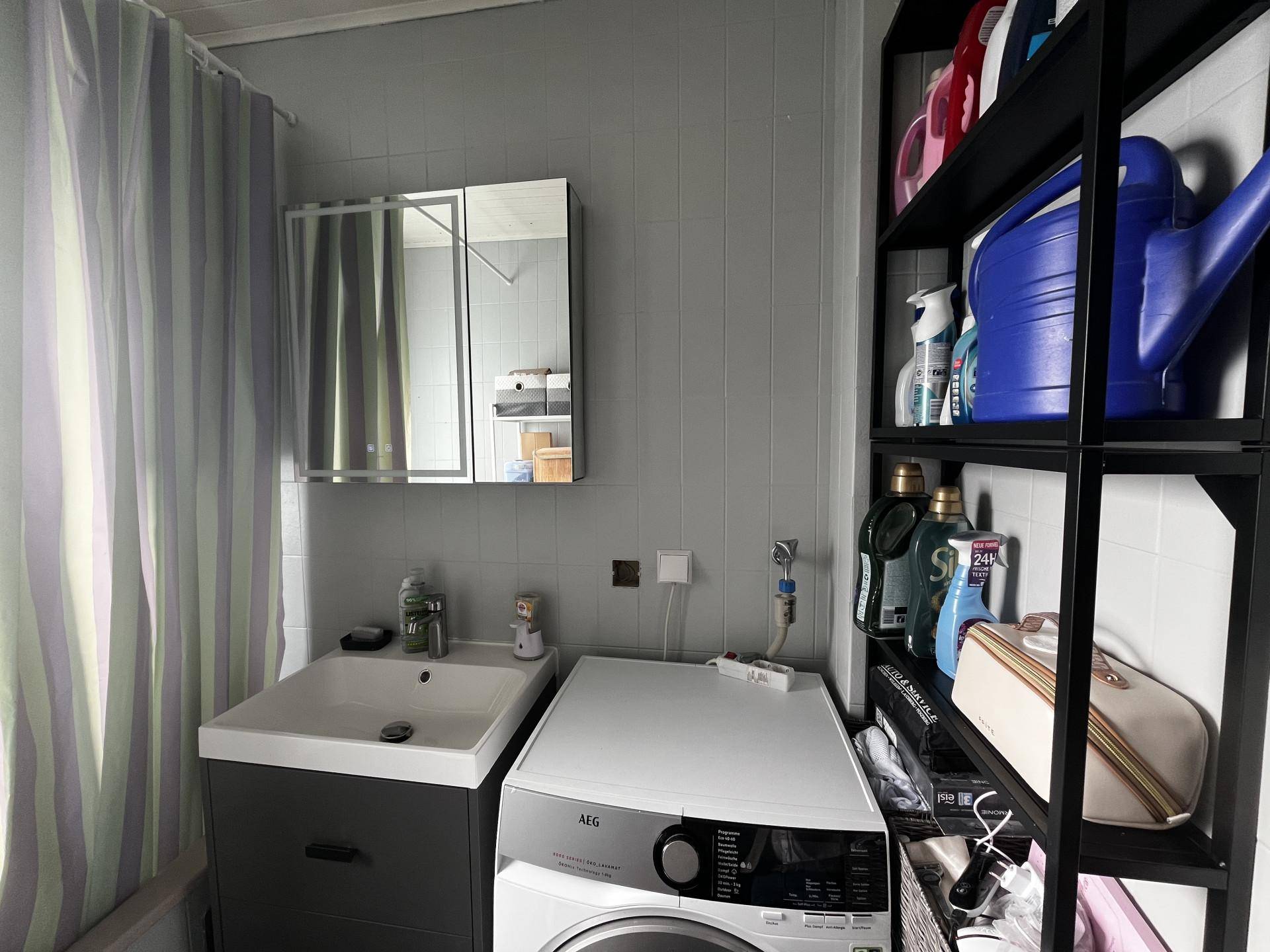 Badezimmer mit Waschmaschine, Waschbecken und praktischen Regalen für Utensilien.