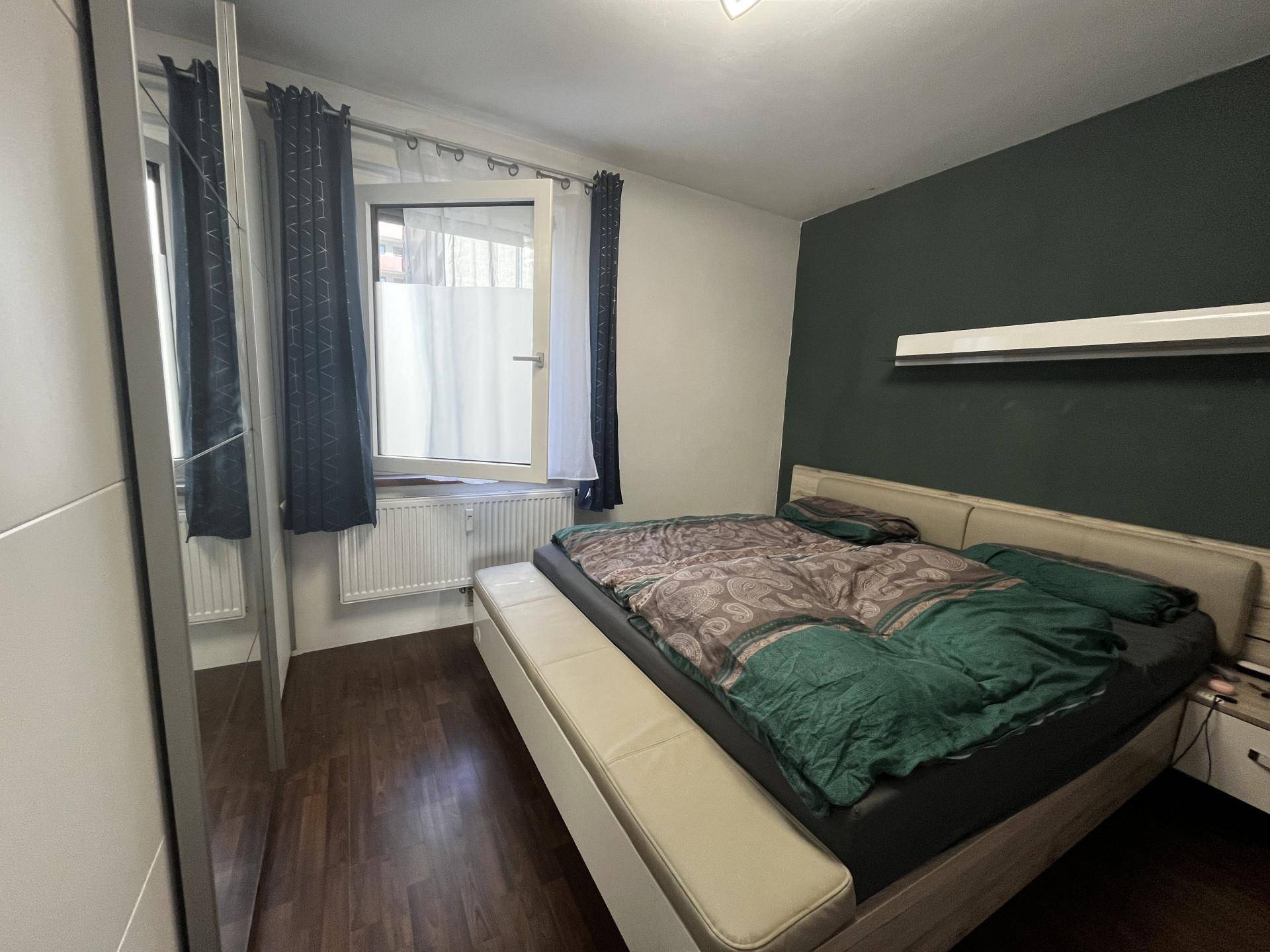 Schlafzimmer mit dunkler Akzentwand, Doppelbett und Holzoptik-Laminatboden.