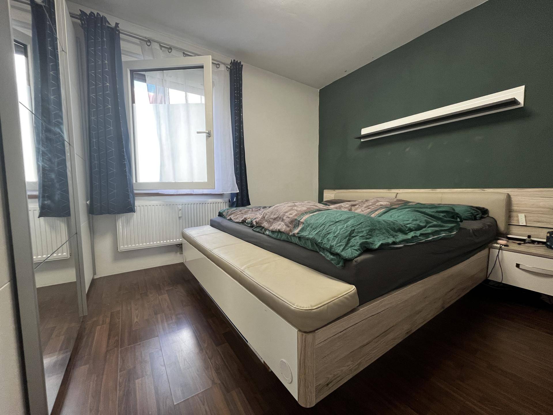 Schlafzimmer mit Doppelbett, dunkler Akzentwand und Fenster.