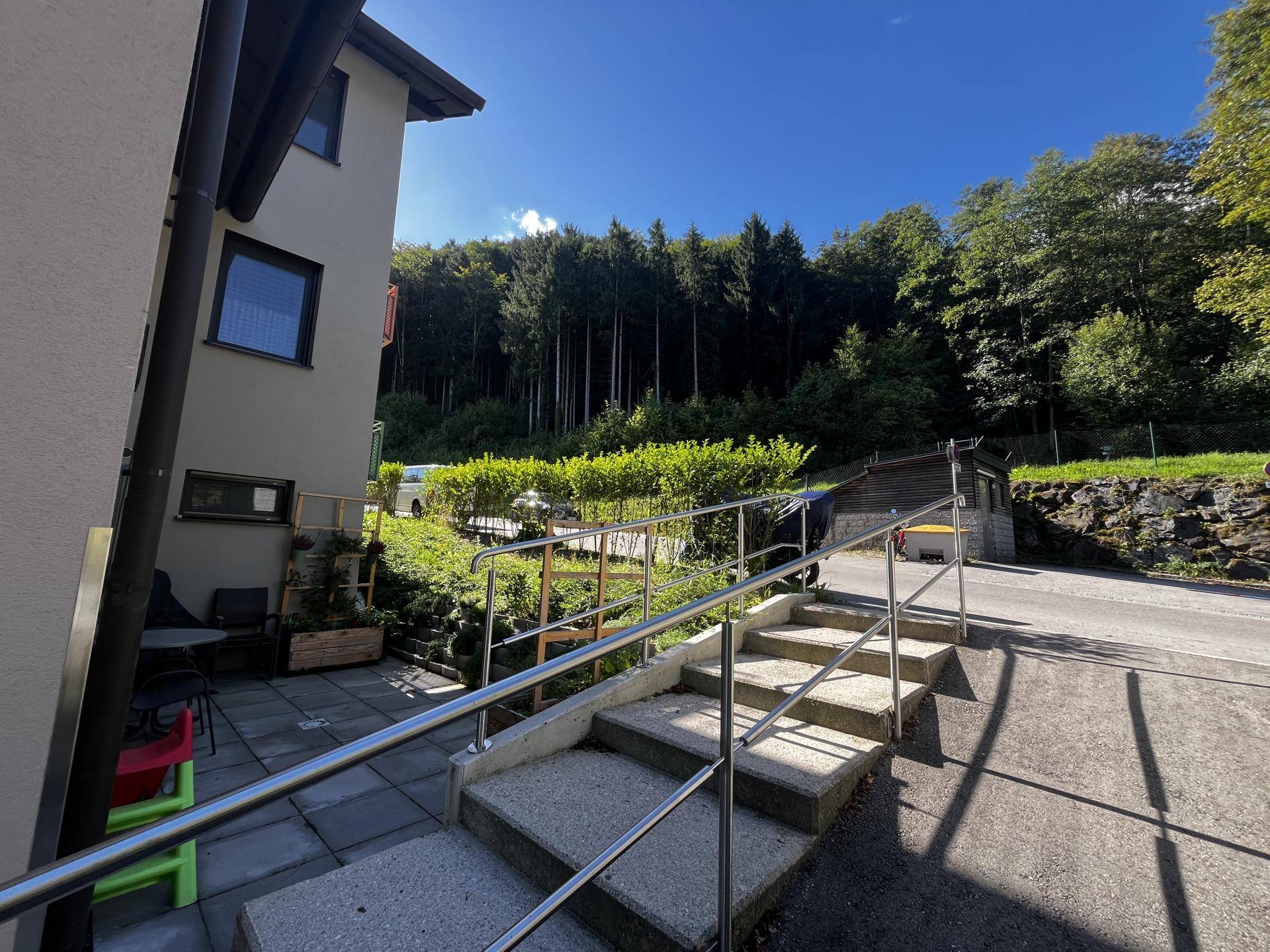 Außentreppe mit Handlauf und Rampe, umgeben von Grünflächen und Bäumen.