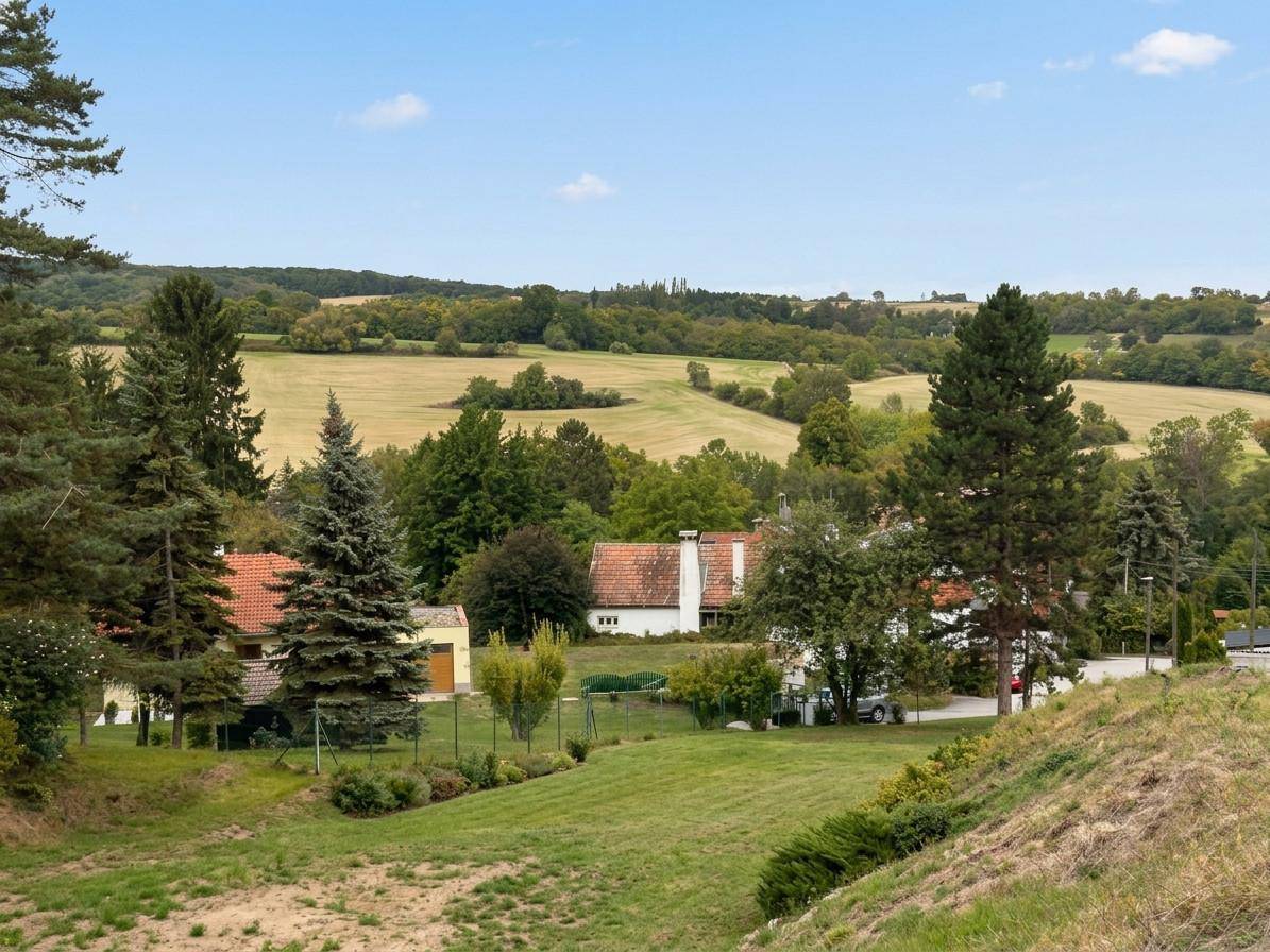 Idyllische Landschaft mit sanften Hügeln, Feldern und vereinzelten Häusern unter klarem Himmel.