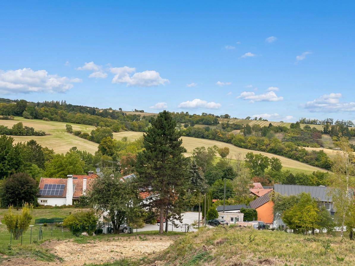 Weitläufiger Blick über eine grüne Hügellandschaft mit einem charmanten Dorf unter blauem Himmel.