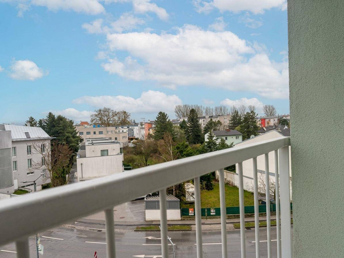Balkon mit Blick auf die umliegende Wohngegend und grüne Bäume unter blauem Himmel.