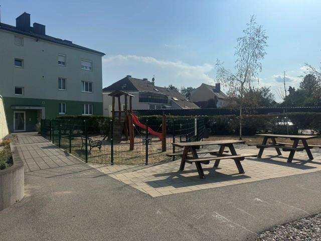 Außenbereich mit Kinderspielplatz, Rutsche und Picknicktischen, umgeben von Grünflächen.