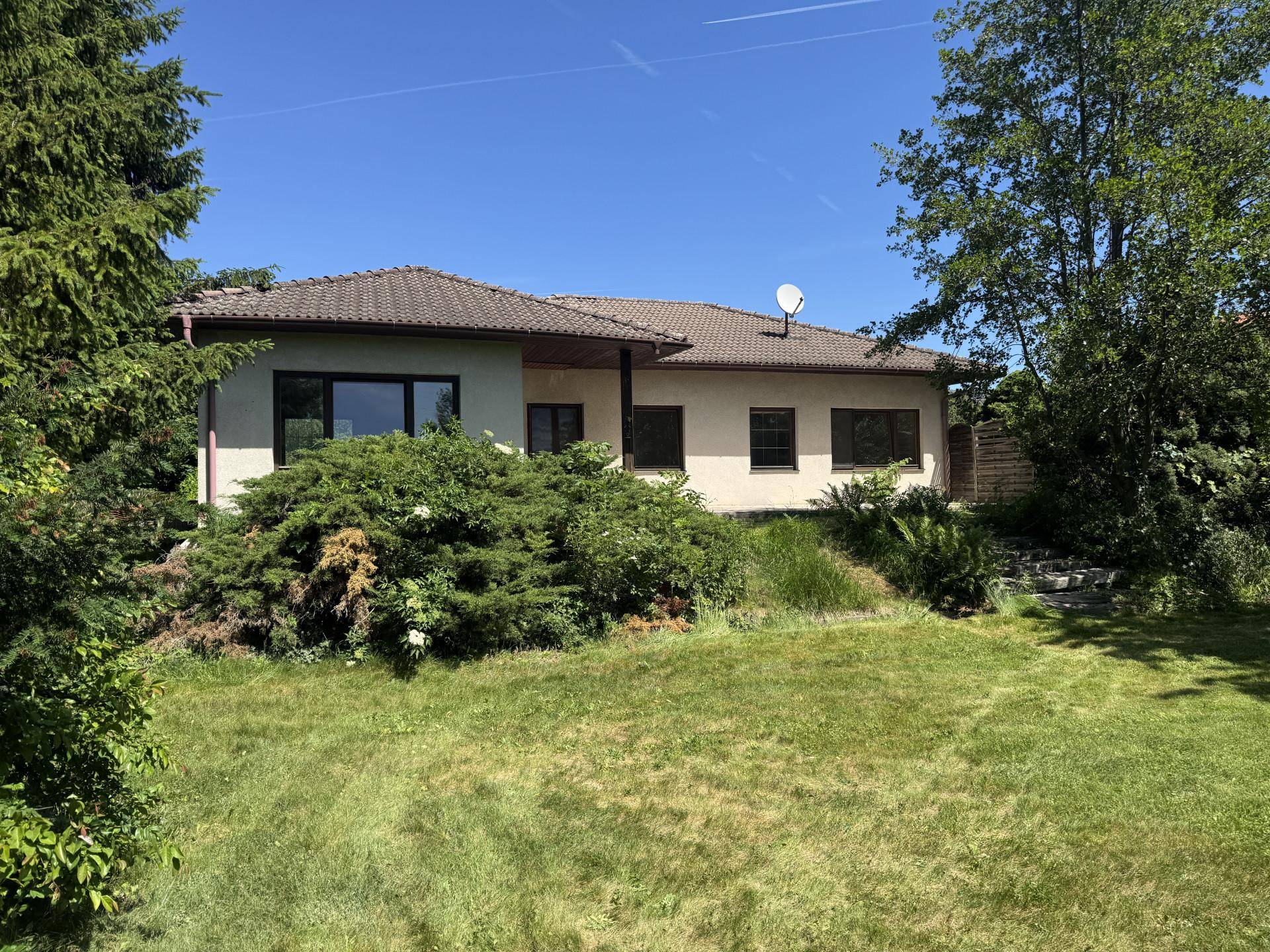 Einfamilienhaus mit heller Fassade und Ziegeldach, umgeben von gepflegtem Rasen und Sträuchern.