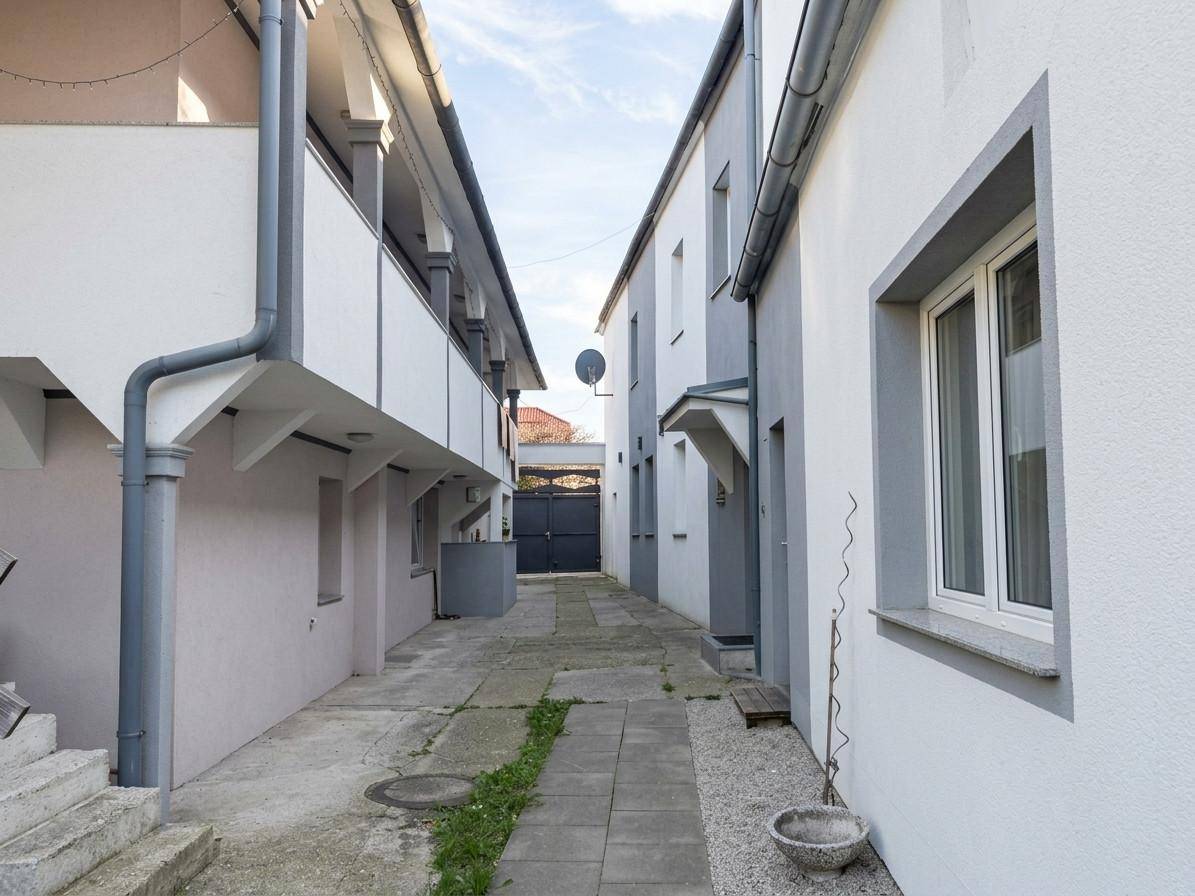 Schmaler gepflasterter Durchgang zwischen zwei Gebäuden, der zu einem Tor führt.