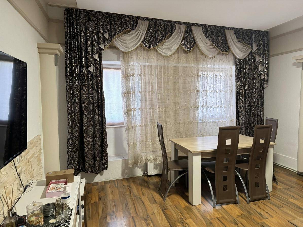 Essbereich mit Holztisch und Stühlen, dekoriert mit opulenten Vorhängen am Fenster.