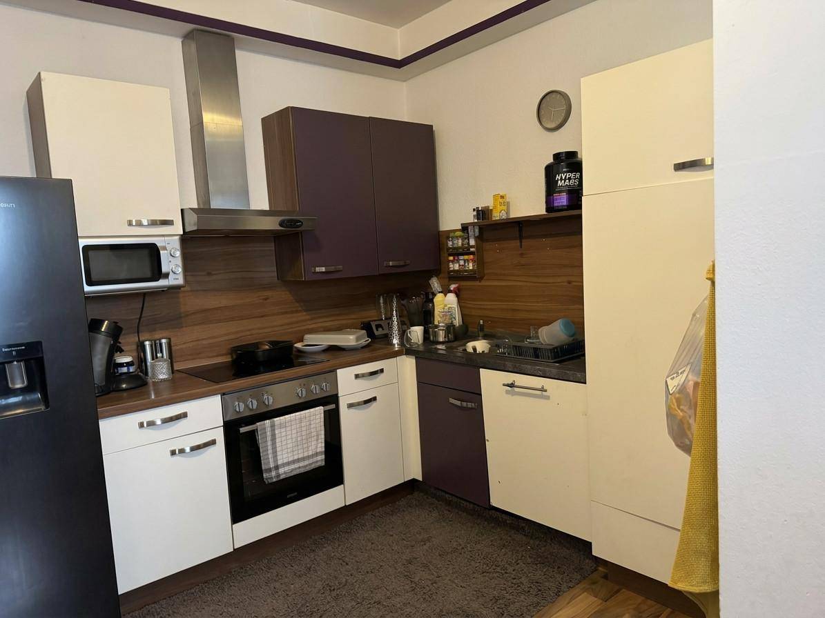 Küche mit weißen und violetten Schränken, ausgestattet mit modernen Geräten und Holzdetails.