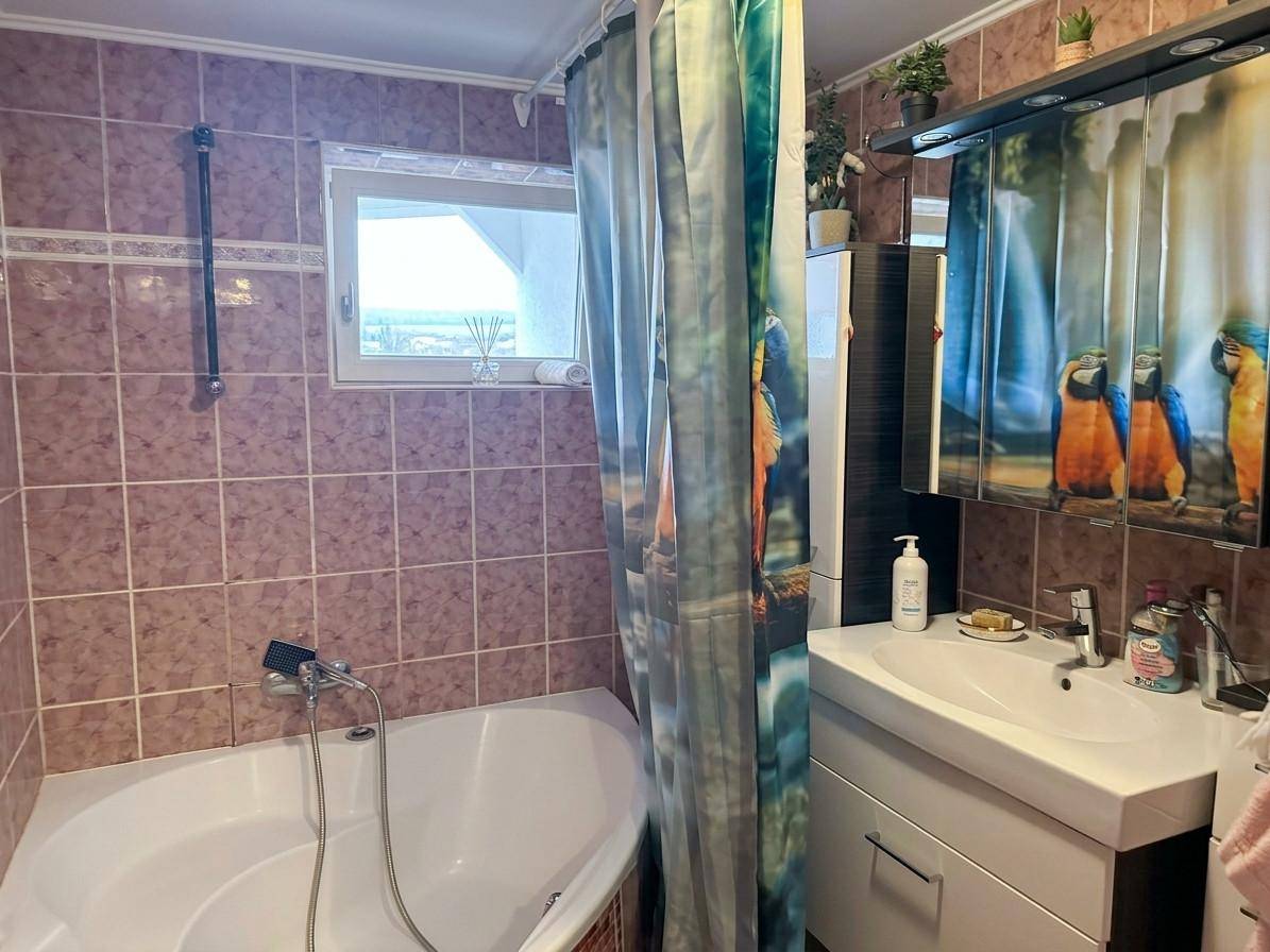 Badezimmer mit rosabraunen Fliesen, Eckbadewanne, Waschbecken und einem Fenster.