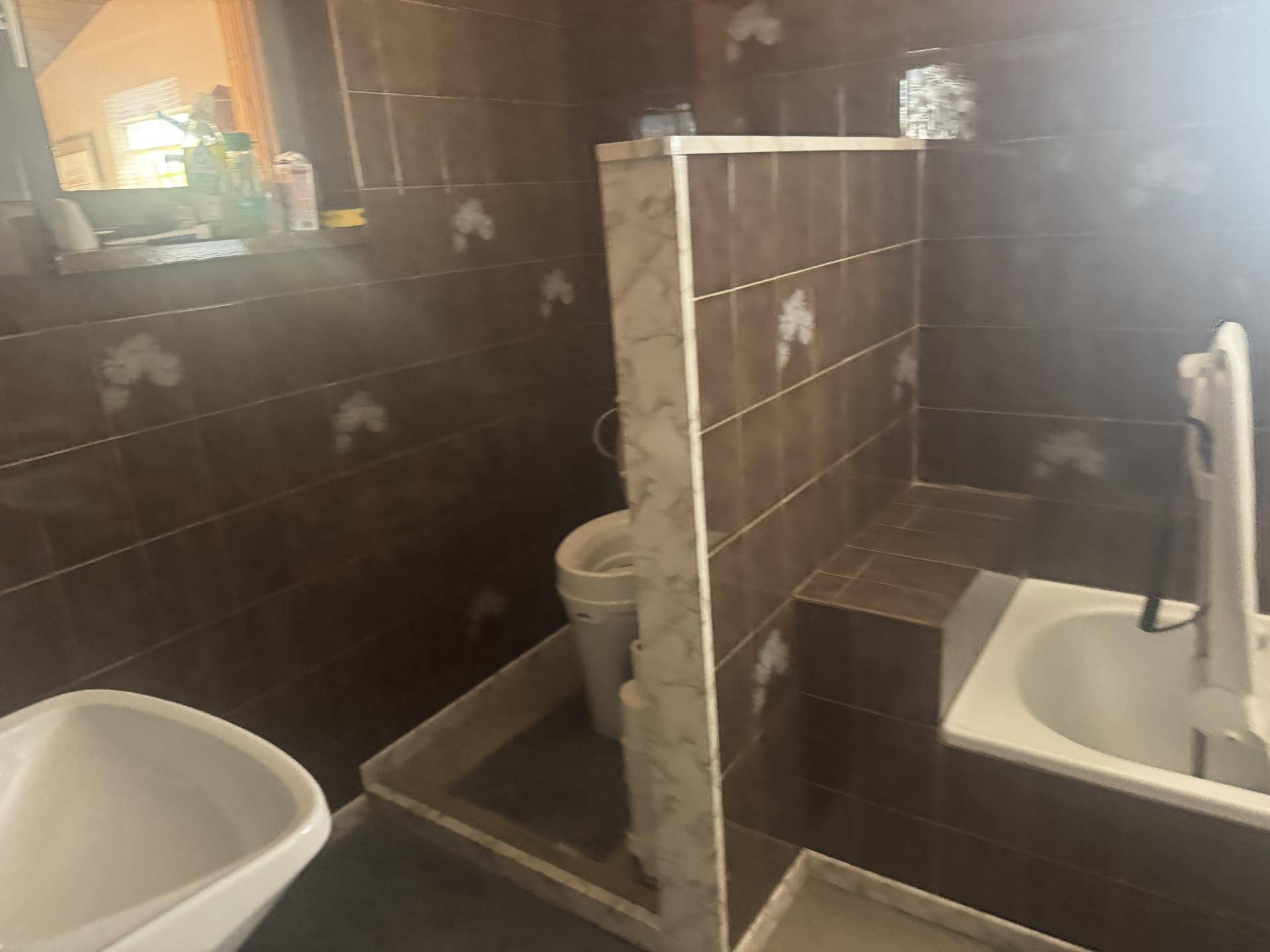 Badezimmer mit braunen Fliesen, einer Badewanne und einem Fenster, ausgestattet mit Haltegriffen.