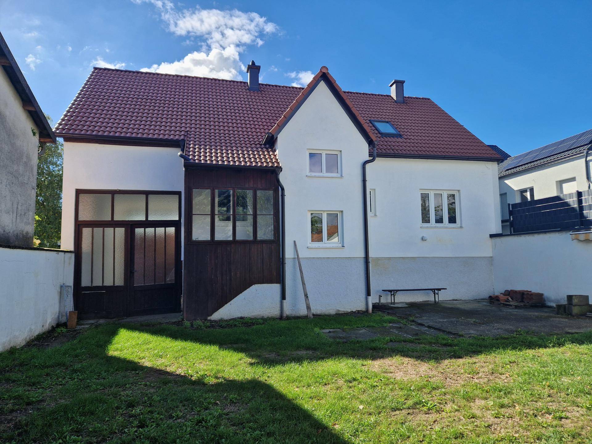 Rückansicht des Hauses mit Anbau und großem Gartenbereich unter blauem Himmel.