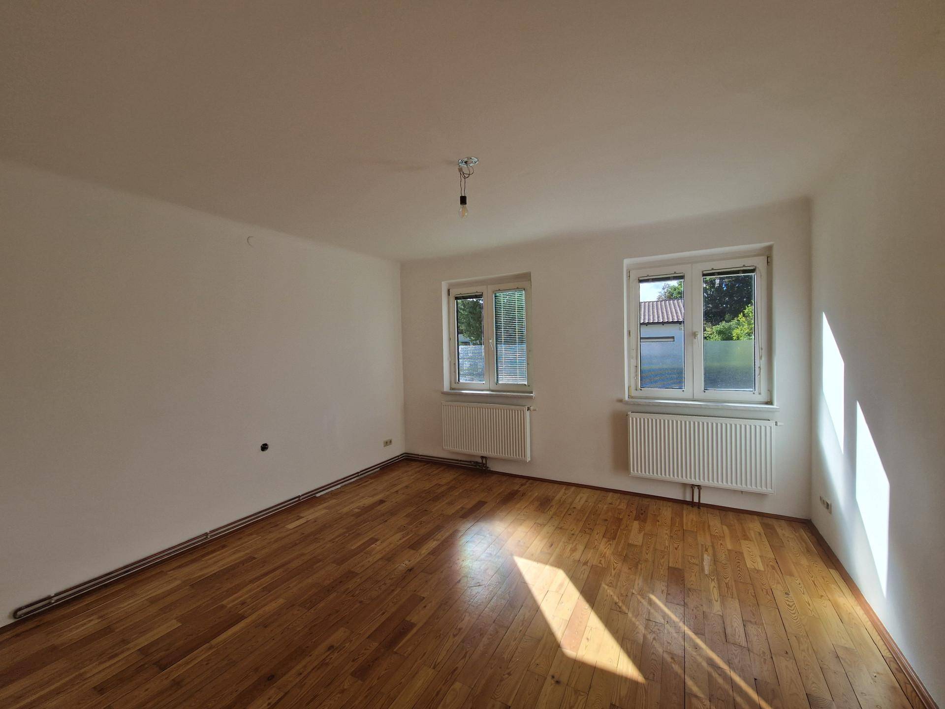 Geräumiges, helles Zimmer mit Parkettboden und zwei Fenstern, die viel Tageslicht hereinlassen.
