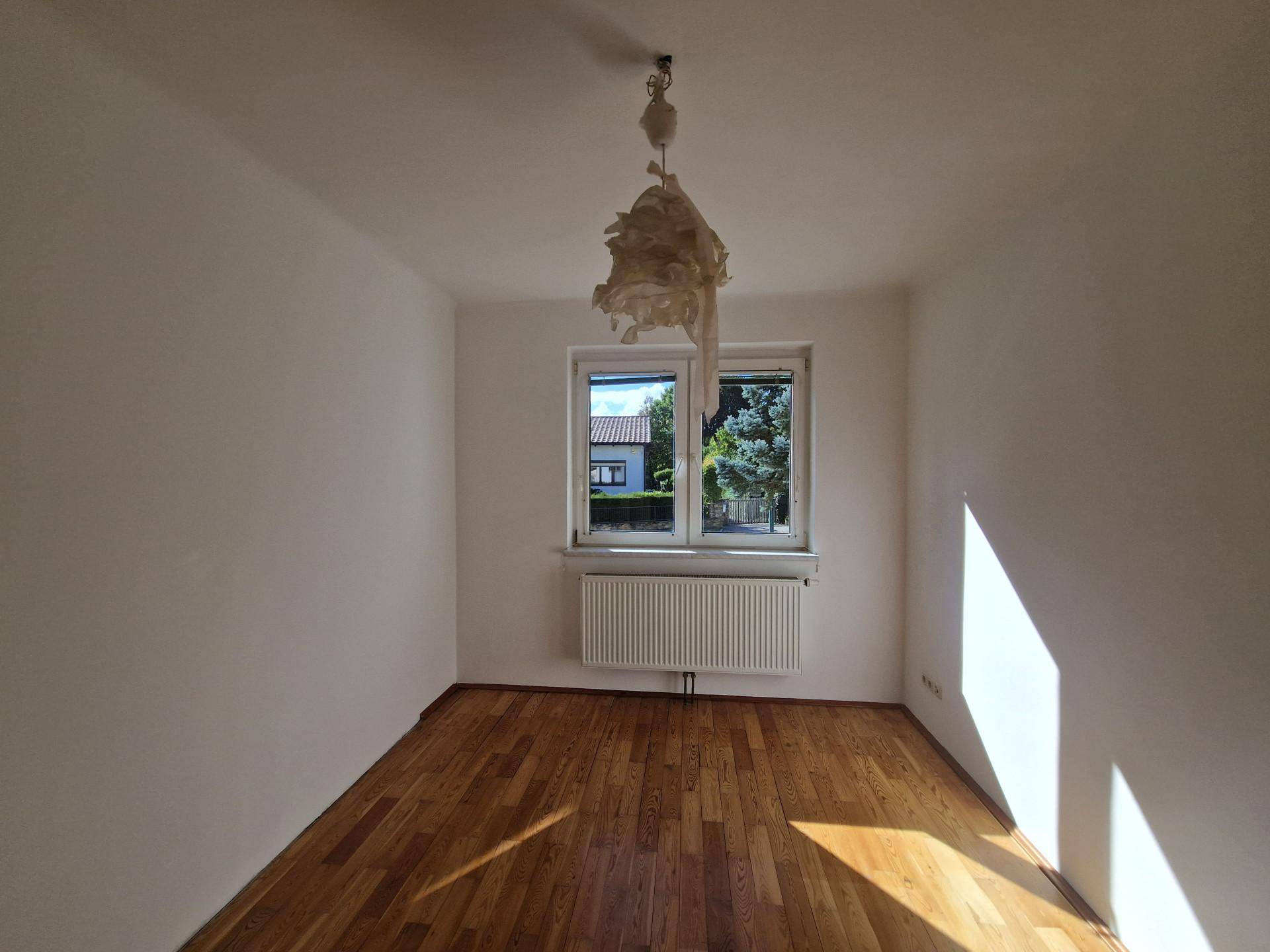 Helles Zimmer mit Parkettboden und einem Fenster, das von der Sonne durchflutet wird.