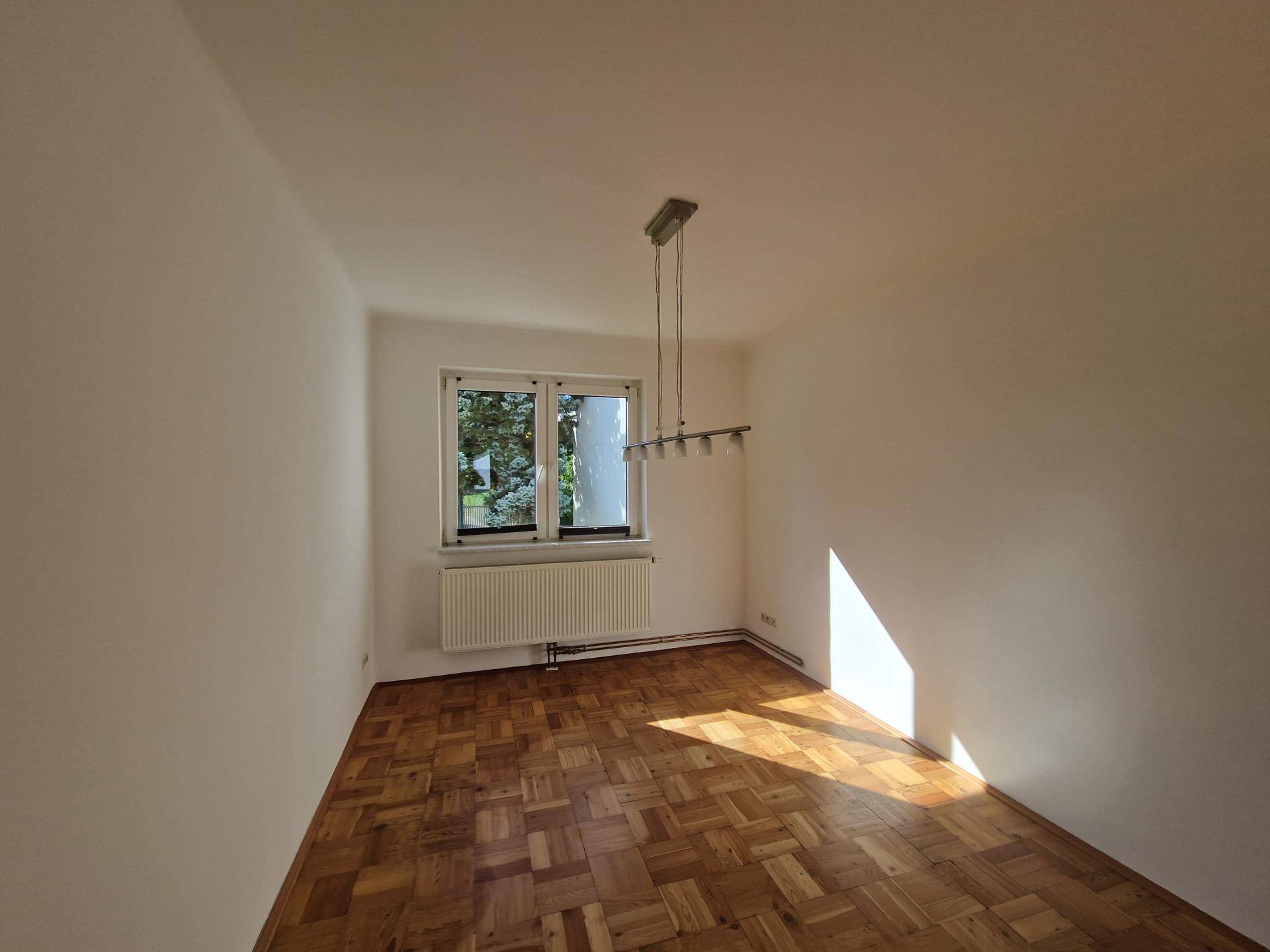Lichtdurchflutetes Zimmer mit Parkettboden und einem Fenster, ideal als Ess- oder Wohnbereich.