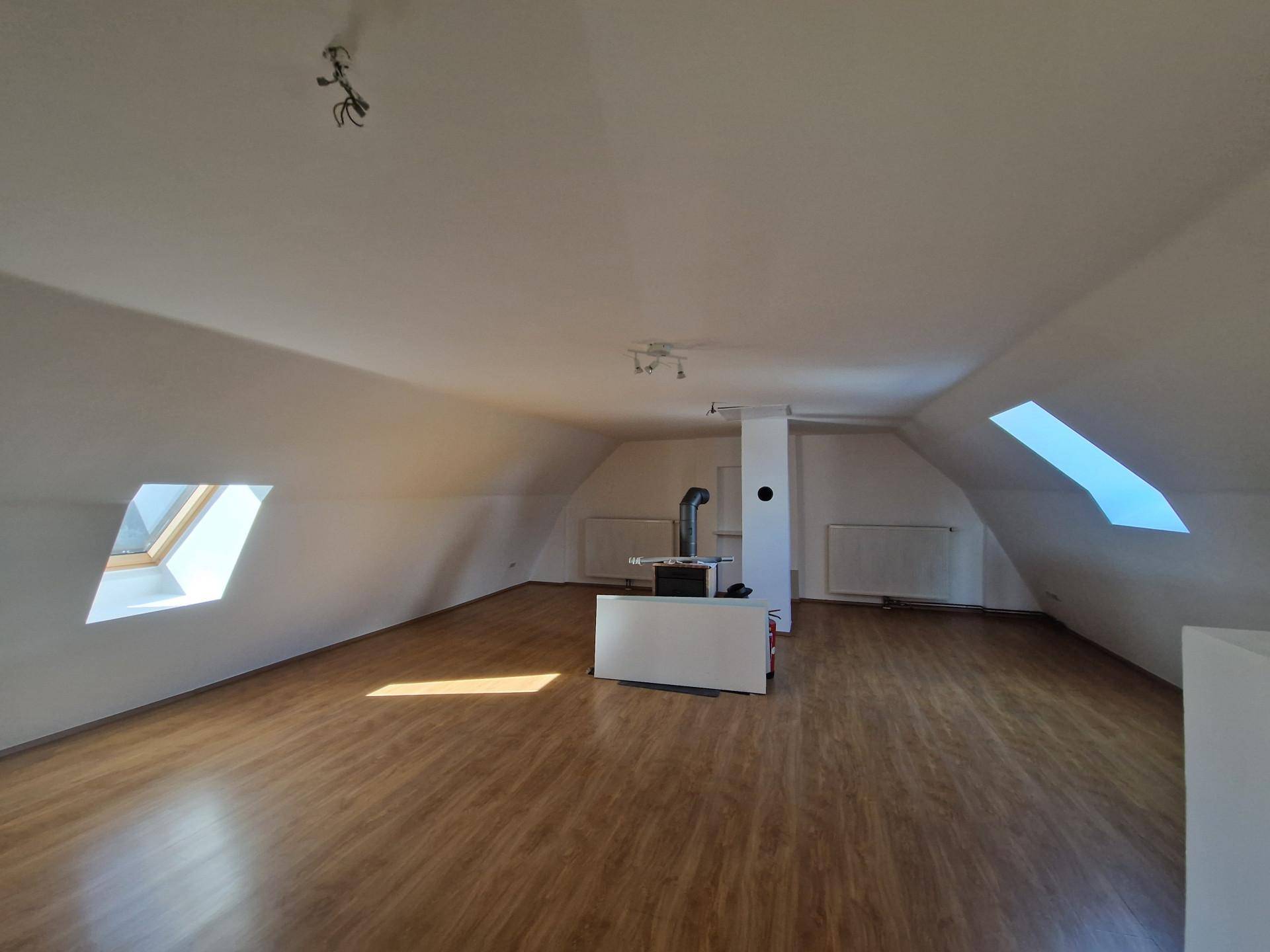 Ausgebauter Dachbodenraum mit Holzboden, Dachschrägen und einem Holzofen in der Mitte.