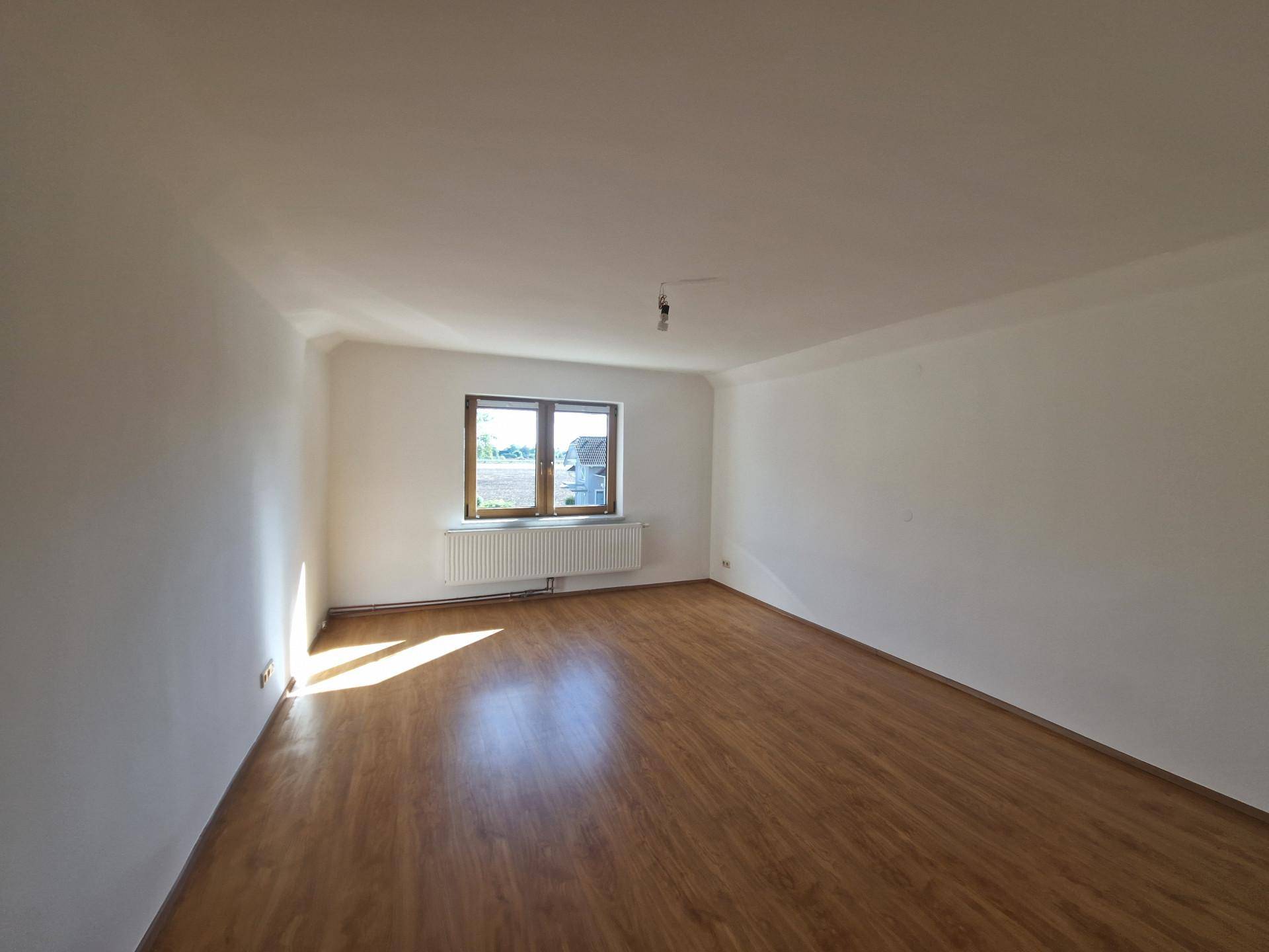 Helles Zimmer mit Laminatboden und einem Fenster, das viel Tageslicht hereinlässt.