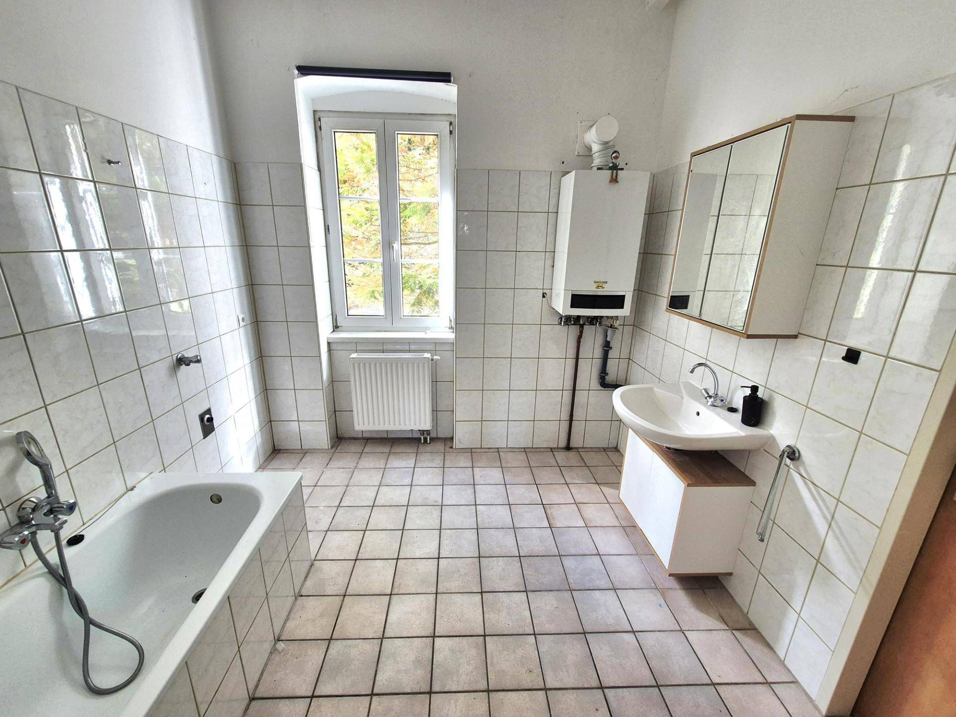 Geräumiges Badezimmer mit Badewanne, Fliesenboden und Fenster, ausgestattet mit Boiler.