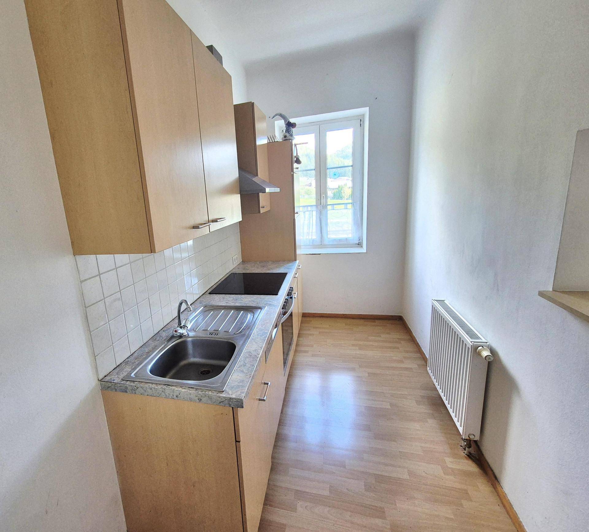 Schmale Küche mit einfacher Einbauküche, Holzdekor und Fenster mit Blick ins Grüne.