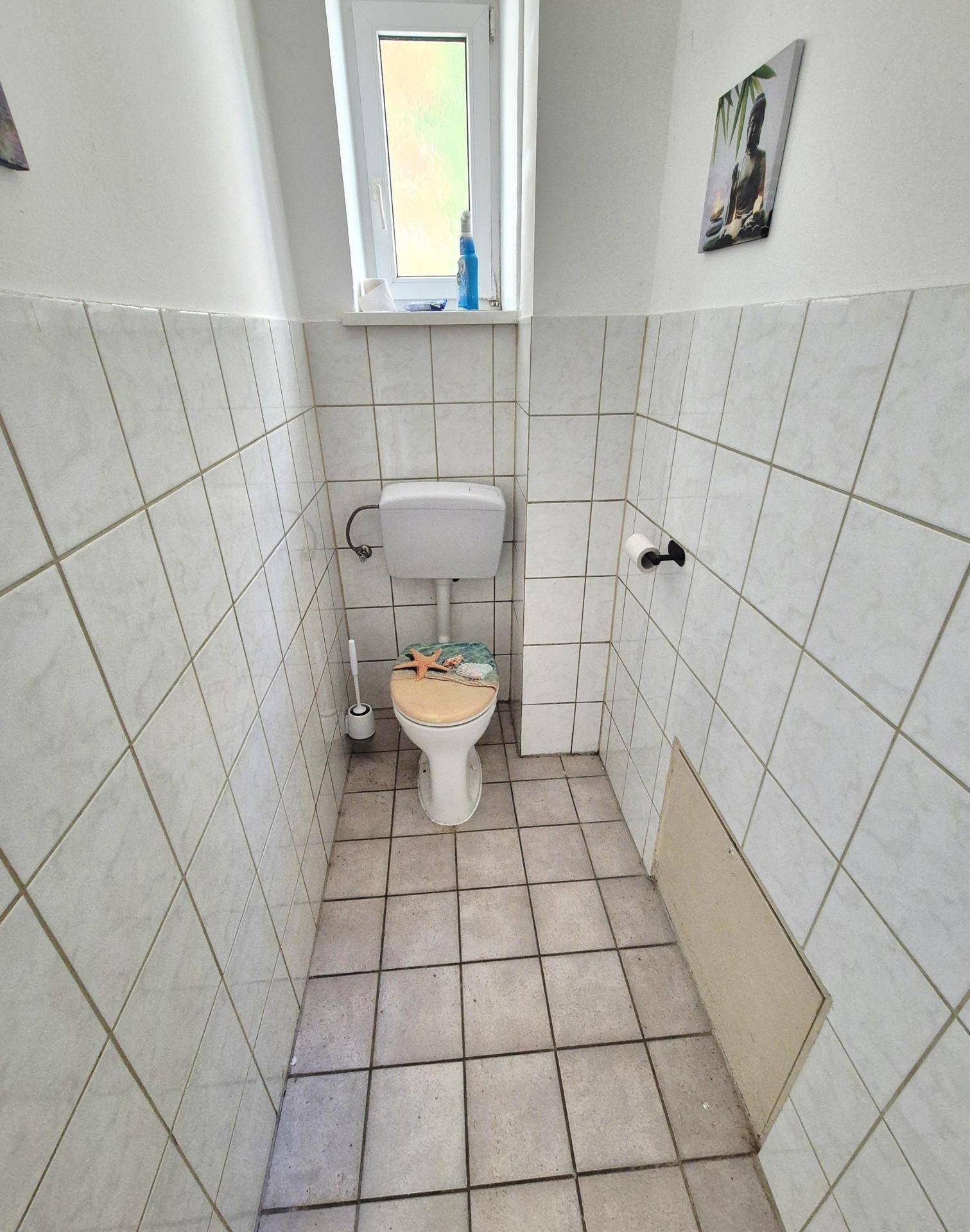 Kleines WC mit Fliesenboden und Fenster, einfach ausgestattet.