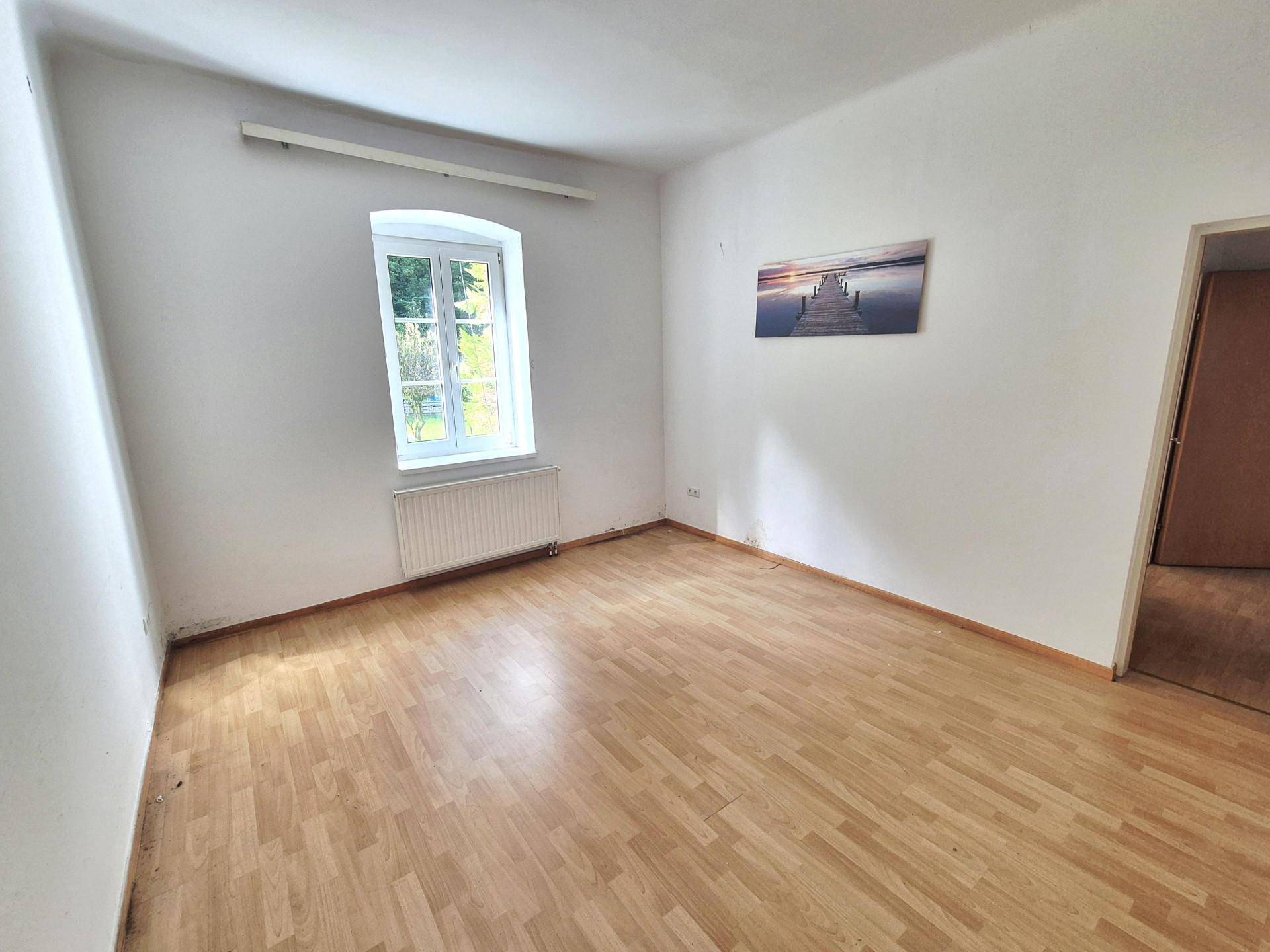 Schlafzimmer mit Laminatboden, weiß gestrichenen Wänden und einem Fenster.