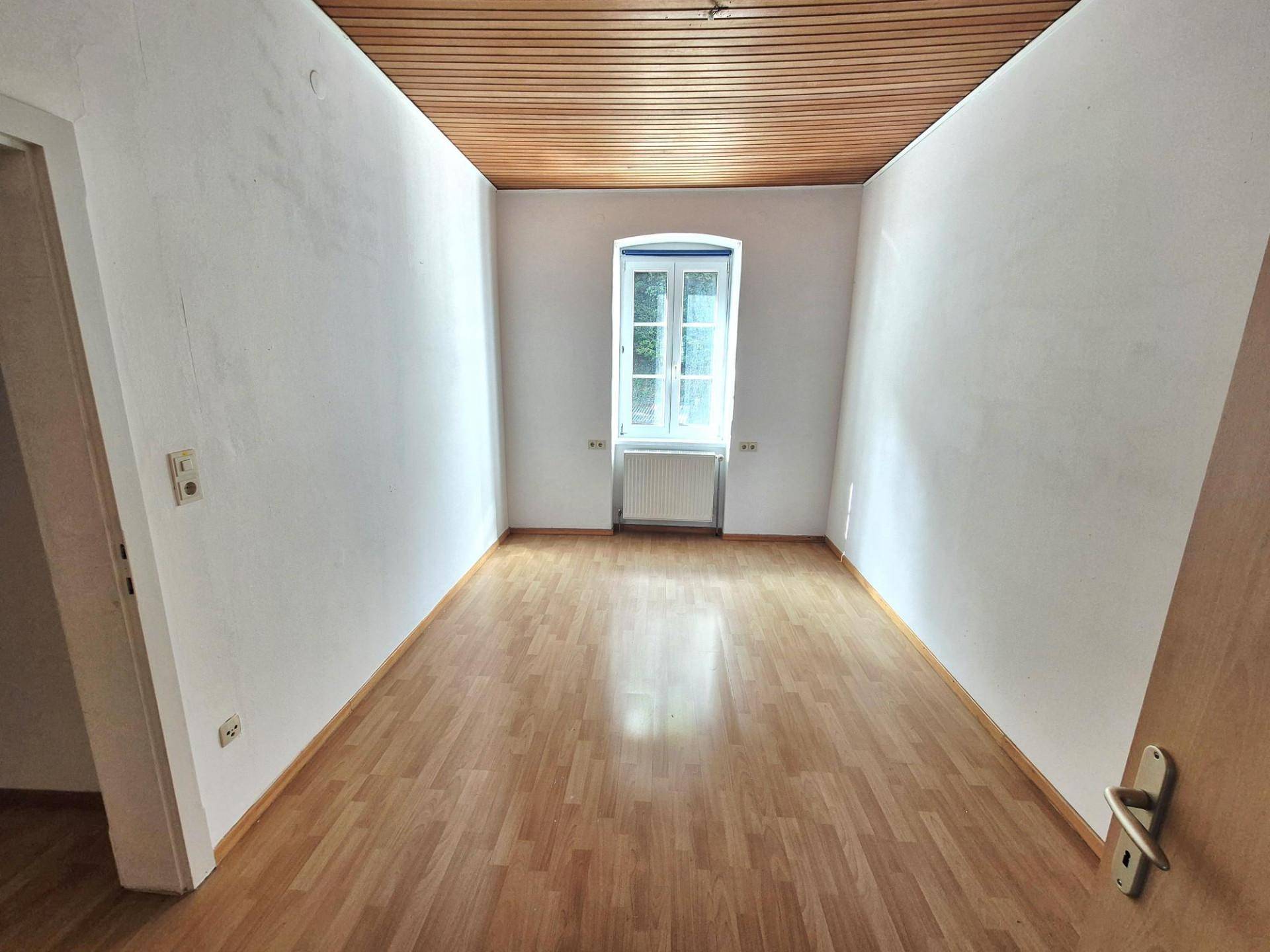 Schlafzimmer mit Holzbalkendecke, Laminatboden und einem Fenster, hell und geräumig.